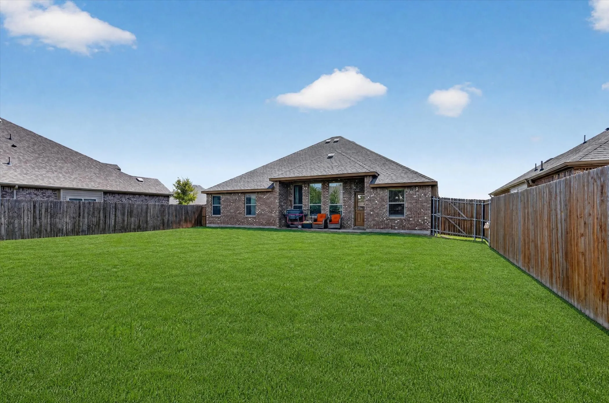 Expansive backyard featuring a manicured lawn, brick exterior, wood privacy fencing, and a paved patio area