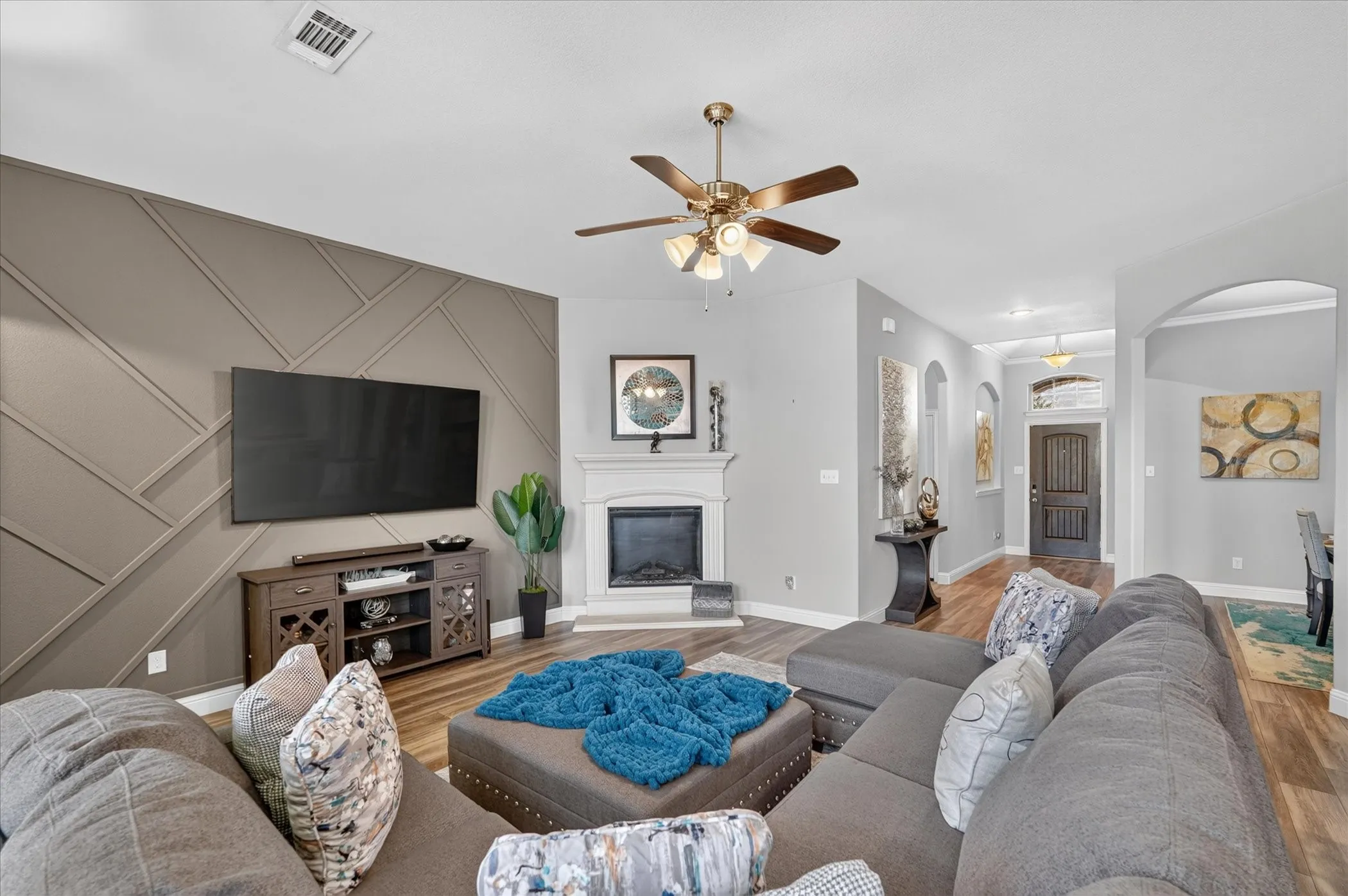 Living space featuring a decorative accent wall, a fireplace with a mantel, wood-finish flooring, and an arched entry