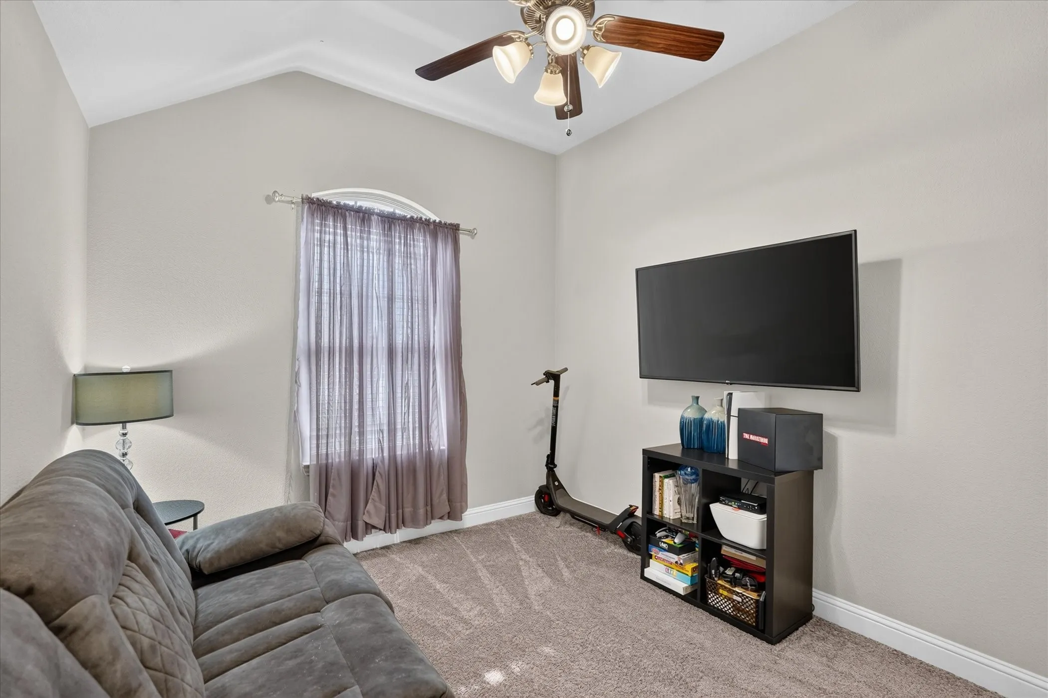 Vaulted ceiling room with an arched window, ceiling fan, and wall-mounted television