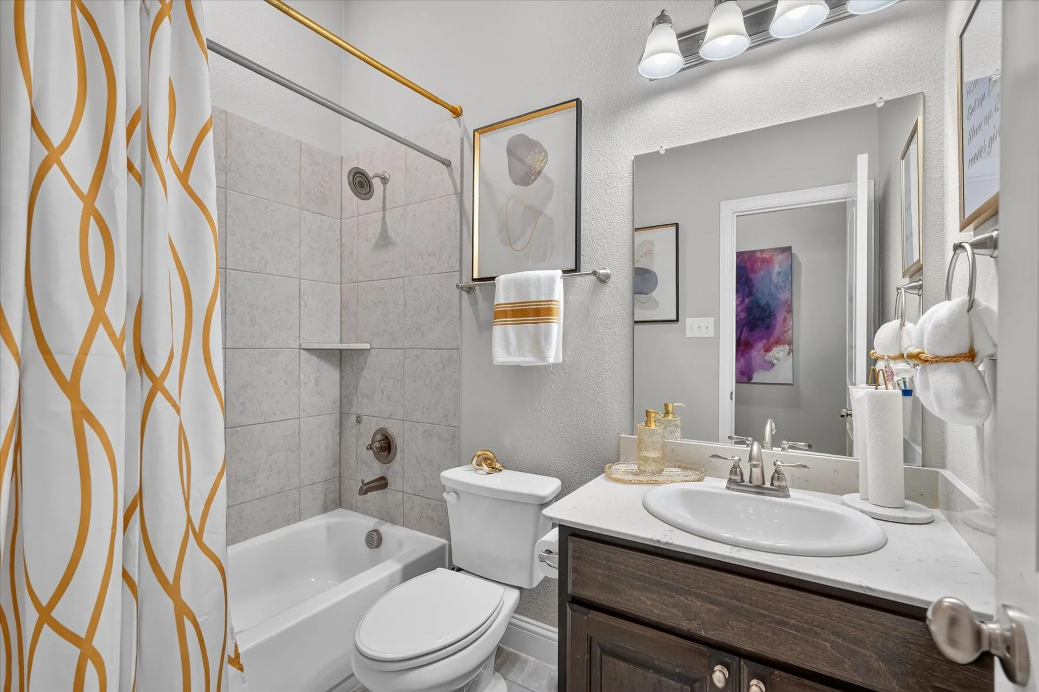 Bathtub with tiled surround, single vanity with integrated sink, dark wood-finish cabinetry, neutral countertop, and wall-mounted mirror