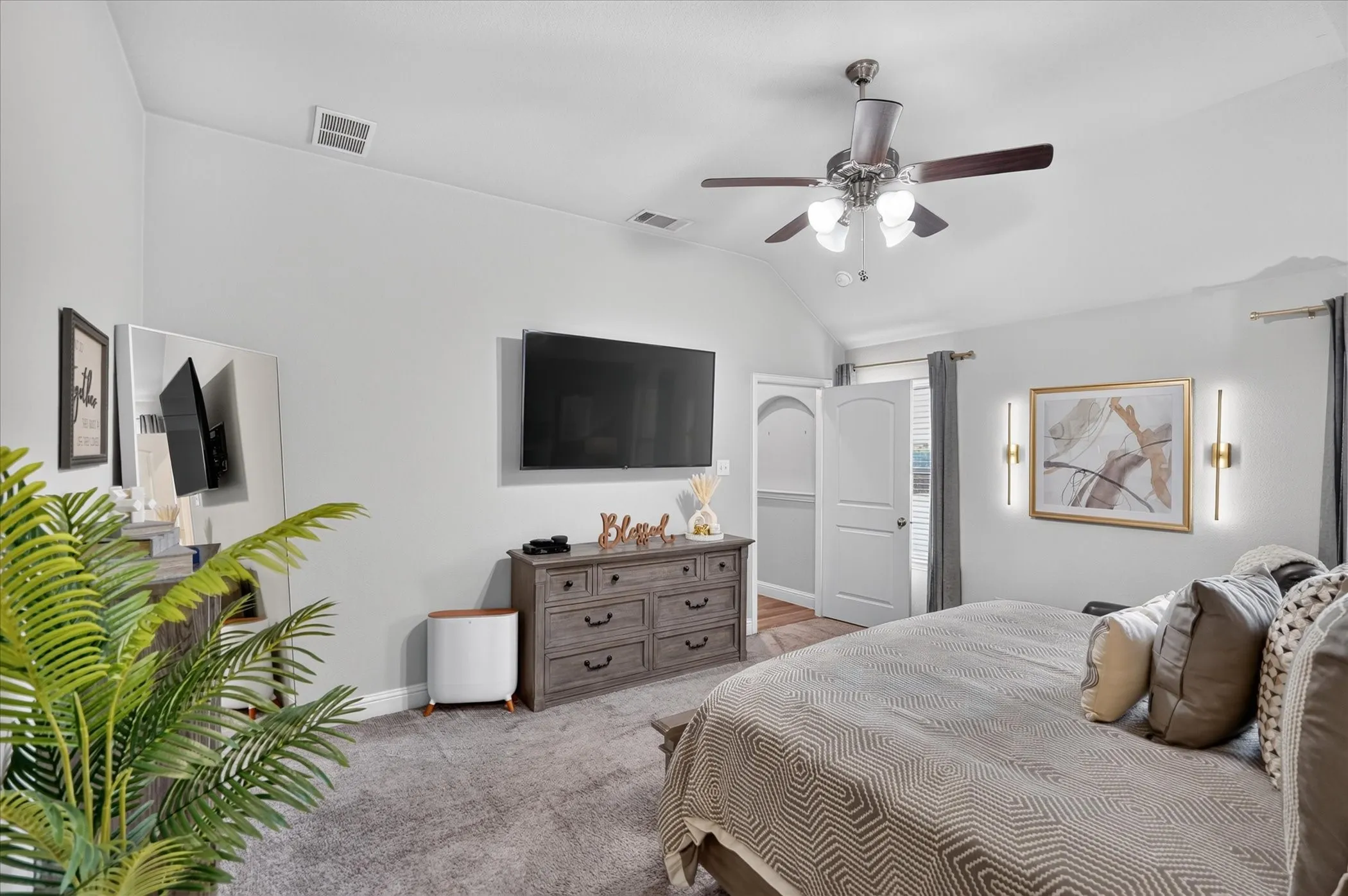 Vaulted ceiling, ceiling fan with integrated lighting, wall-mounted light fixtures, arched doorway, and soft gray carpeting
