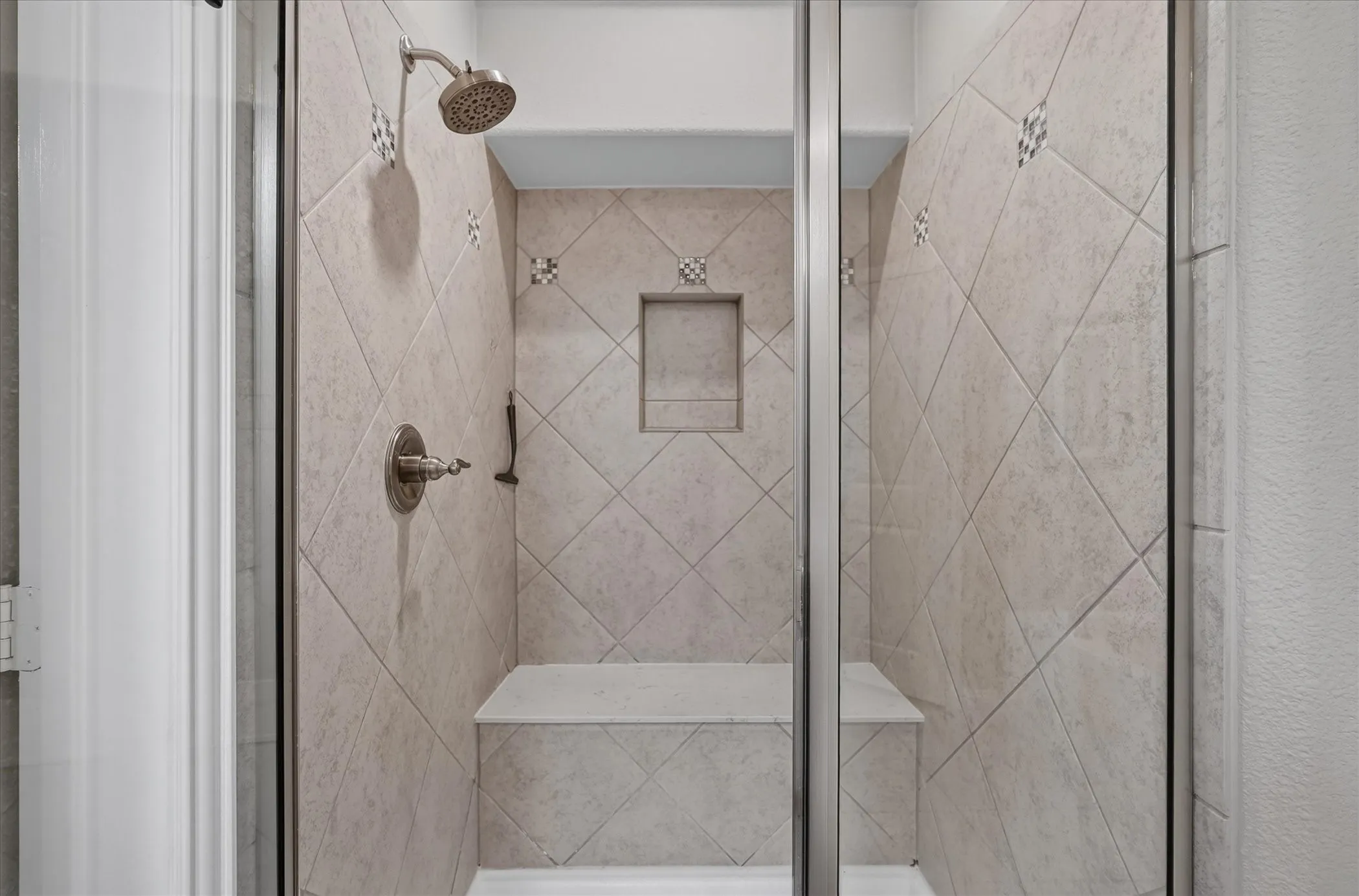 Glass-enclosed shower featuring diagonal tile work, a built-in shower niche, a built-in bench, and a brushed nickel showerhead and fixtures
