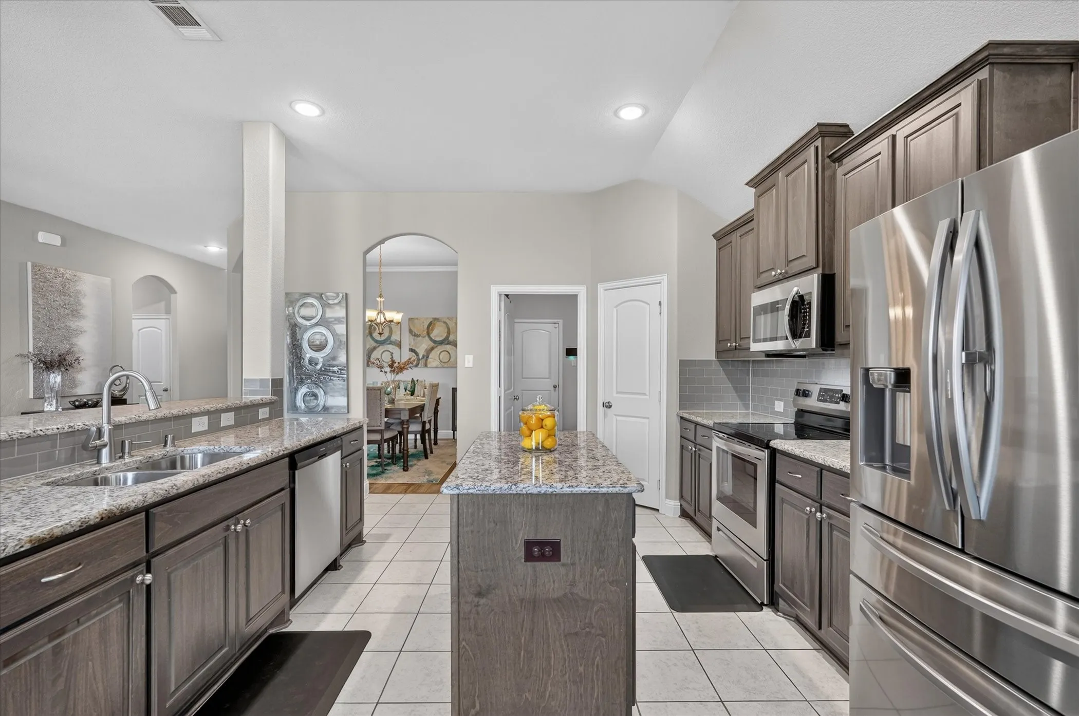 Kitchen featuring stainless steel appliances, granite countertops, a tile backsplash, wood-finish cabinetry, and an island with a breakfast bar