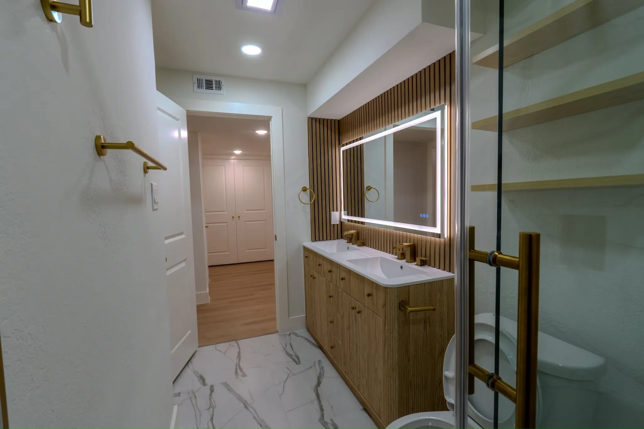 Dual vanity with an illuminated mirror, wood-finish cabinetry, and gold-finish fixtures