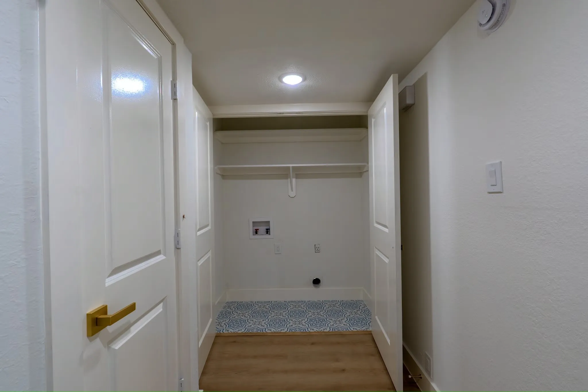Dedicated laundry area with upper shelving, wood-finish flooring, and a patterned floor mat
