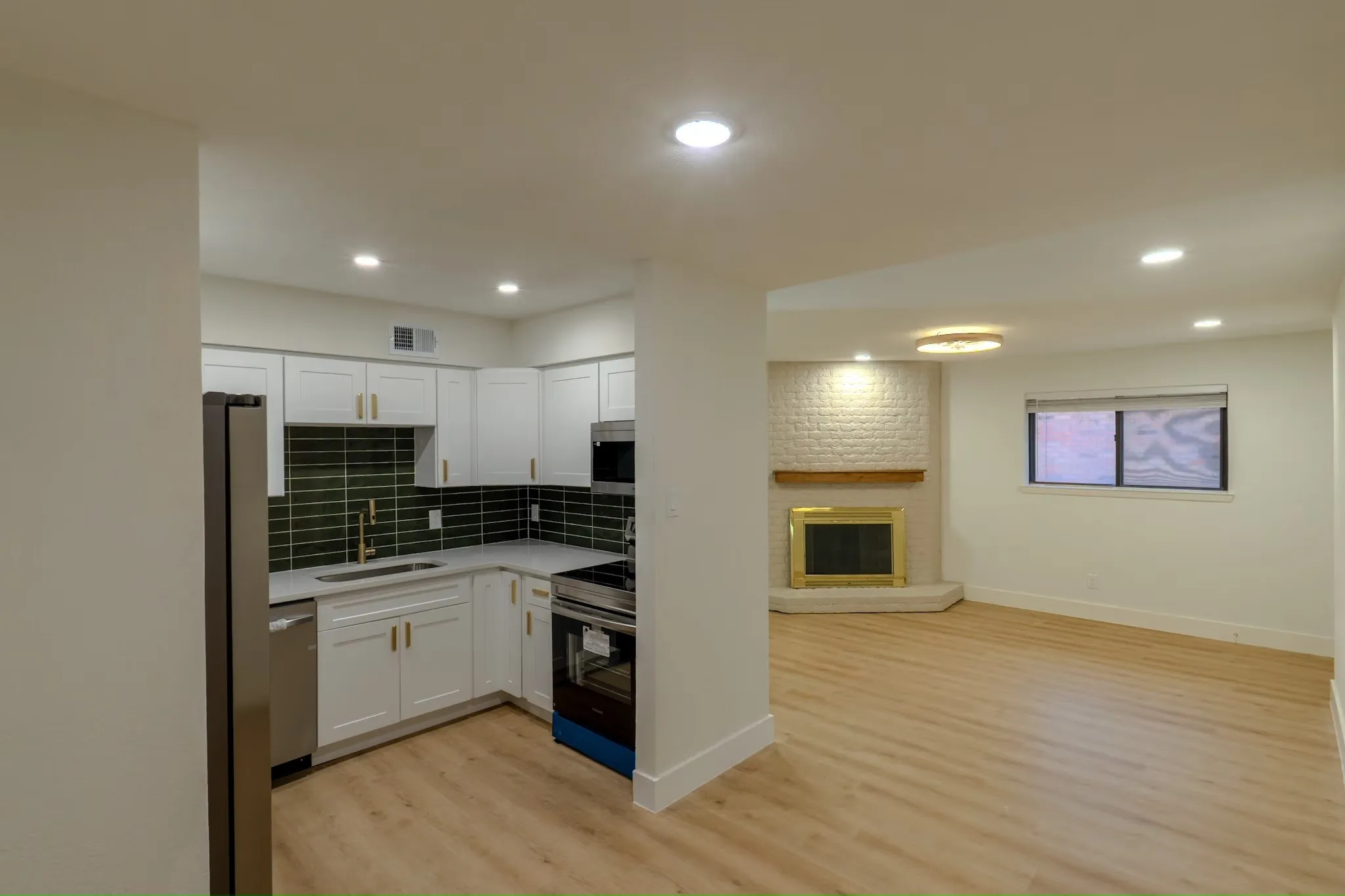 White shaker cabinetry with gold-tone hardware, stainless steel appliances, dark green subway tile backsplash, and light wood-finish flooring