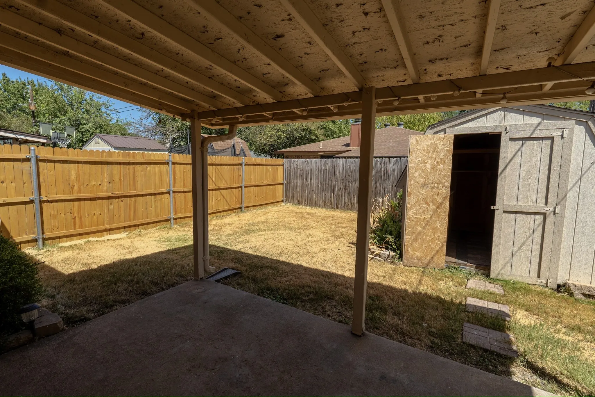Covered patio with a concrete surface, wooden privacy fencing, and a detached storage shed