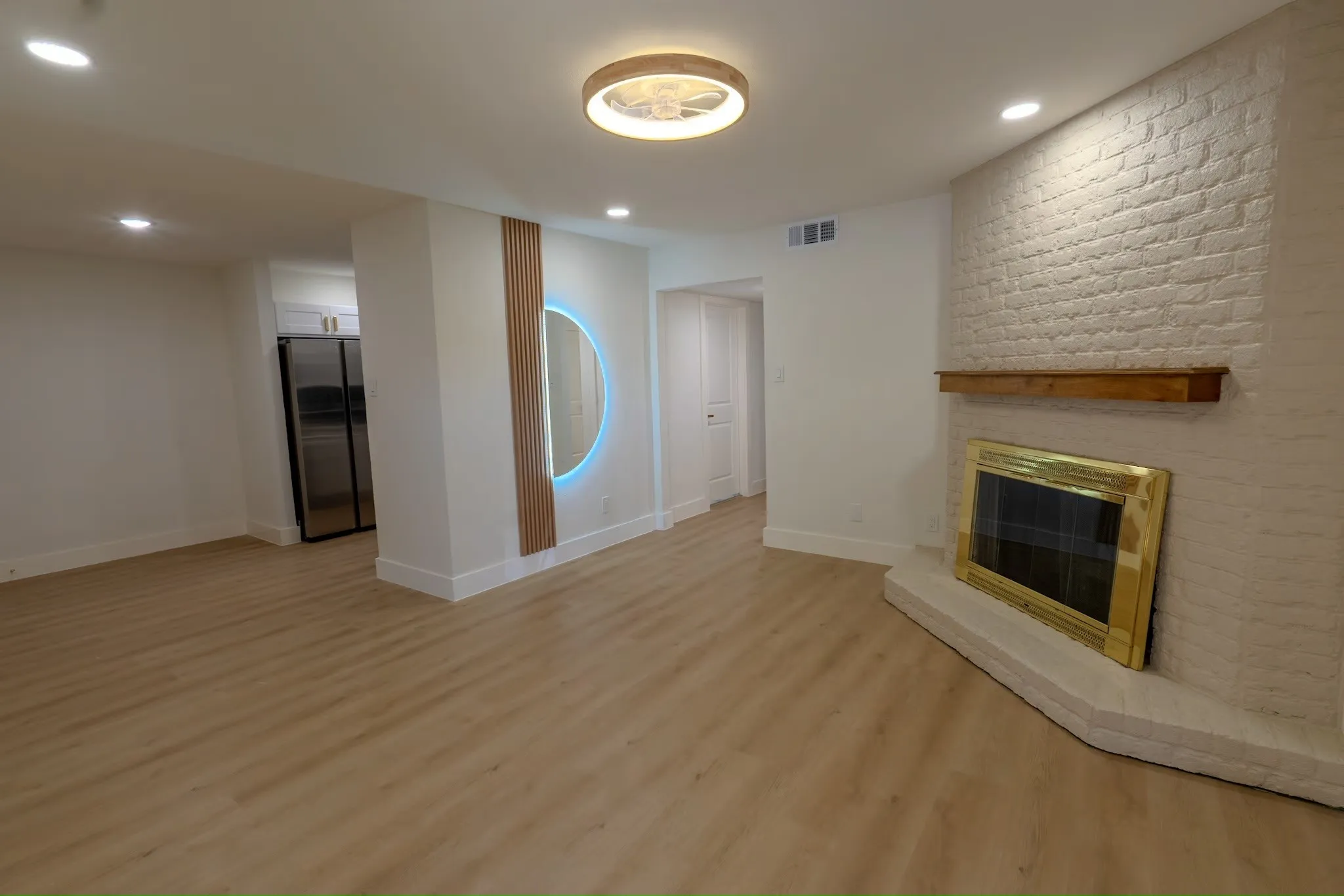 Spacious room featuring wood-finish flooring, a white brick fireplace with a wood mantel, and recessed lighting