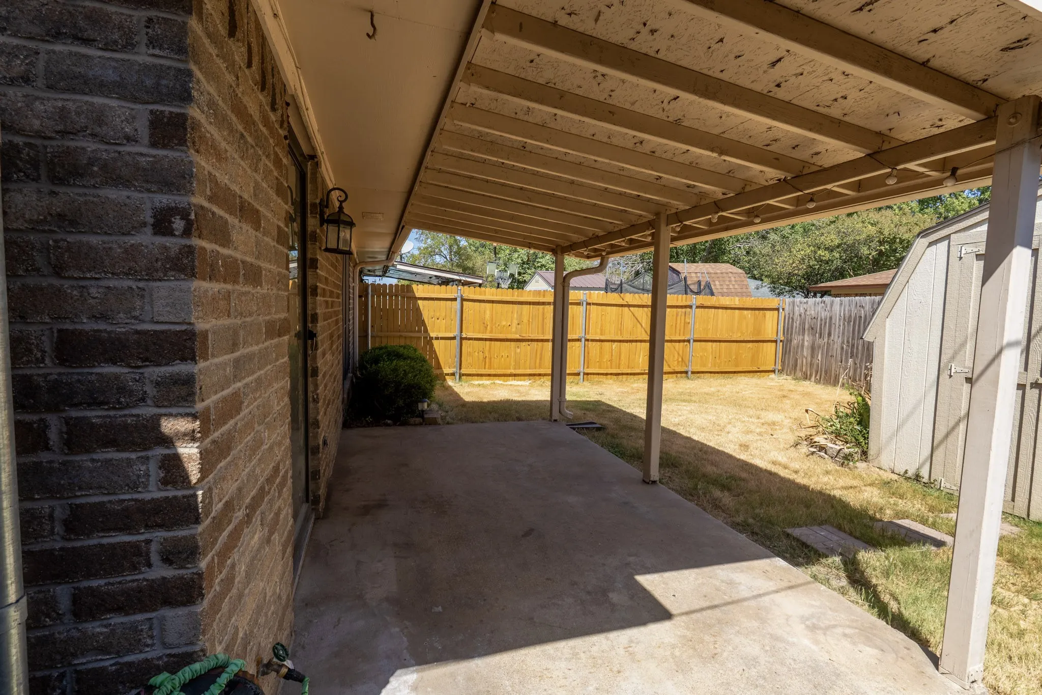 Covered patio with a concrete surface, brick exterior, built-in outdoor lighting, and wood privacy fencing