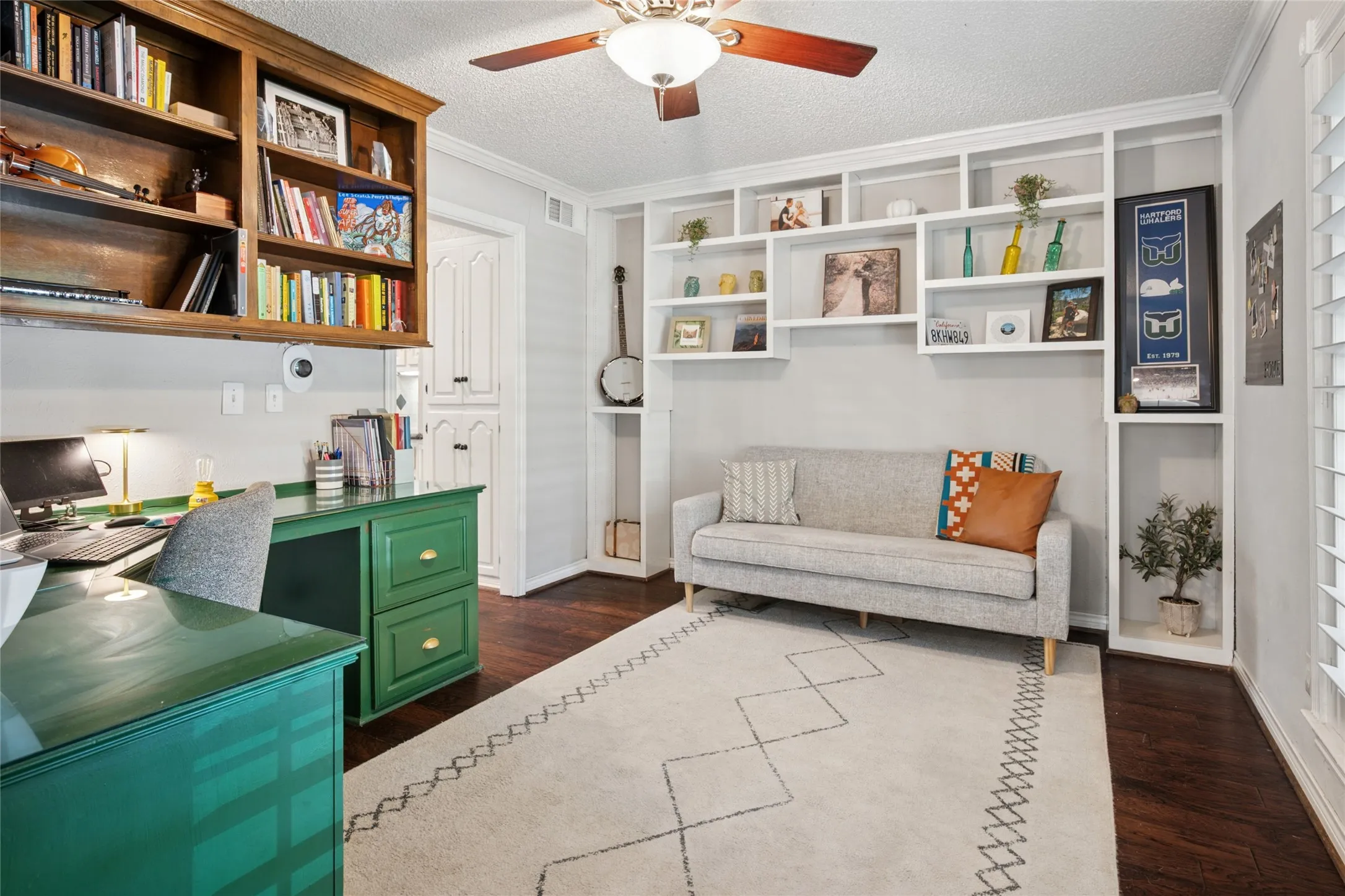Office space with wood floors, a ceiling fan, and built-ins in the sitting area and desk area