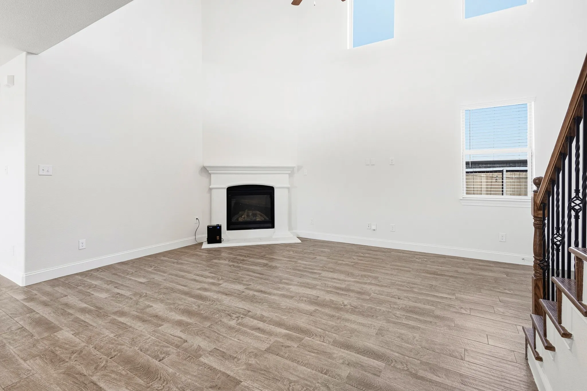 Vaulted ceiling, wood-finish flooring, white fireplace with mantle, window with blinds, and staircase with wrought iron balusters