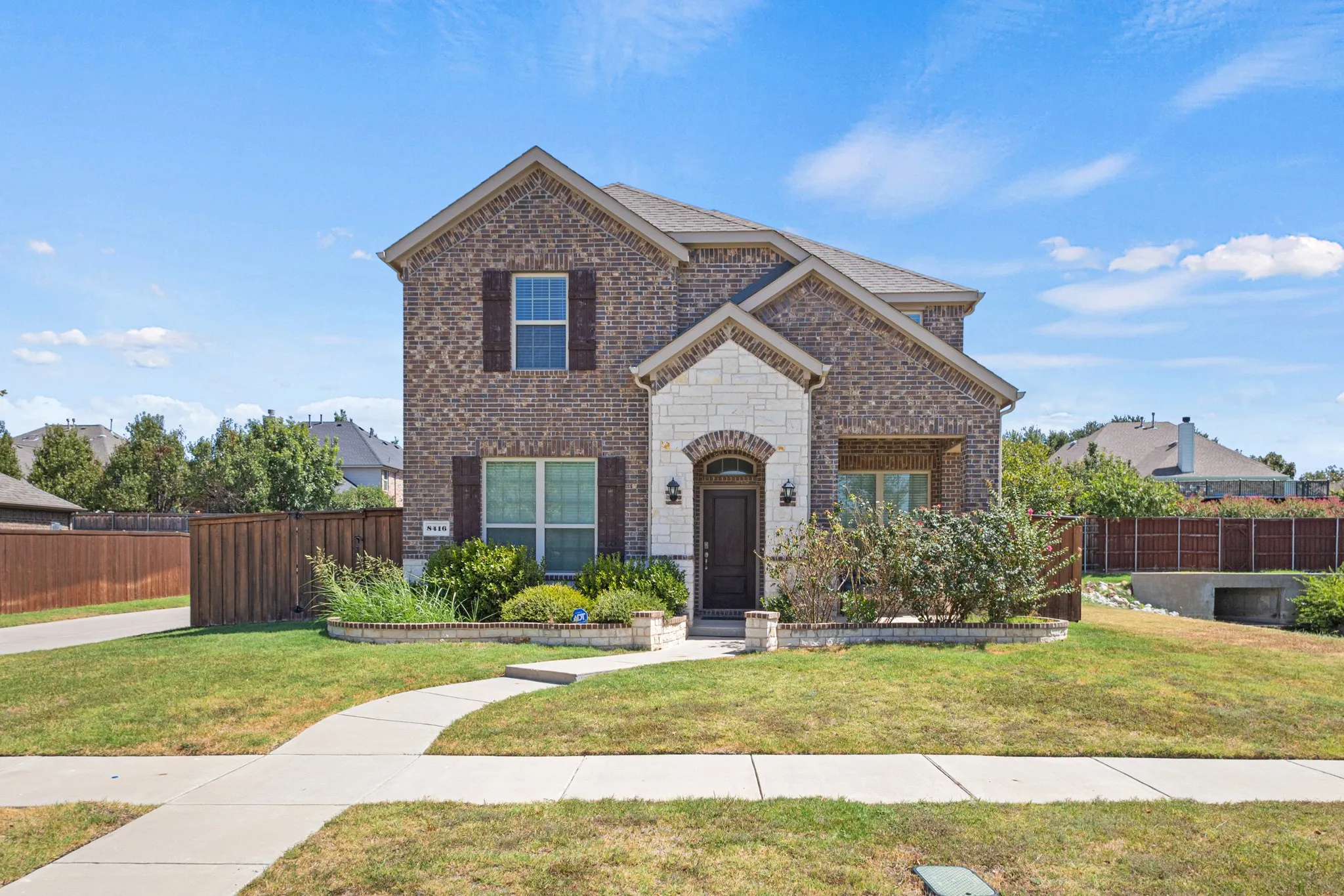 Brick exterior with stone accents, arched entryway, dark wood front door, decorative shutters, and mature landscaping