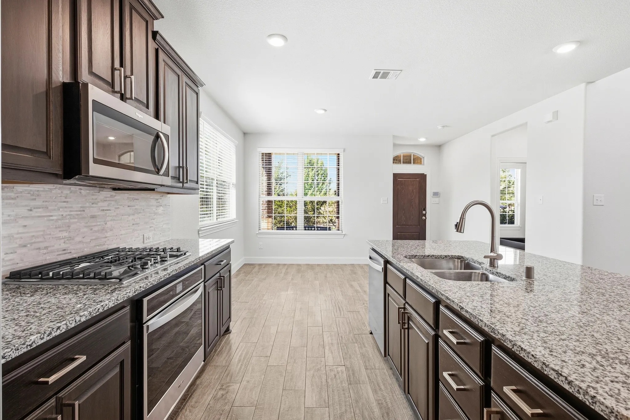 Granite countertops, stainless steel appliances, wood-finish flooring, dark wood cabinetry, and a gas range