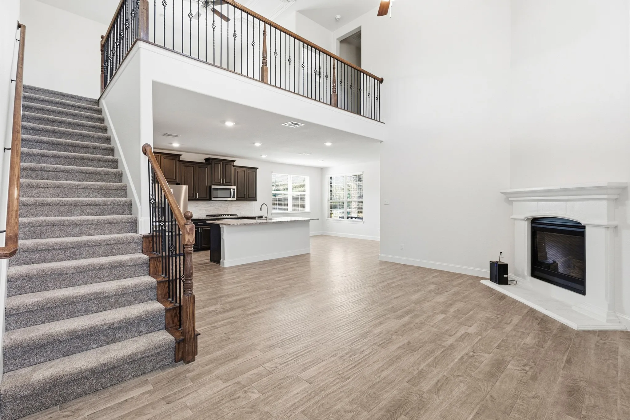 Open-concept living area featuring wood-finish flooring, a gas fireplace with white surround, and a kitchen with white cabinetry and stainless steel appliances
