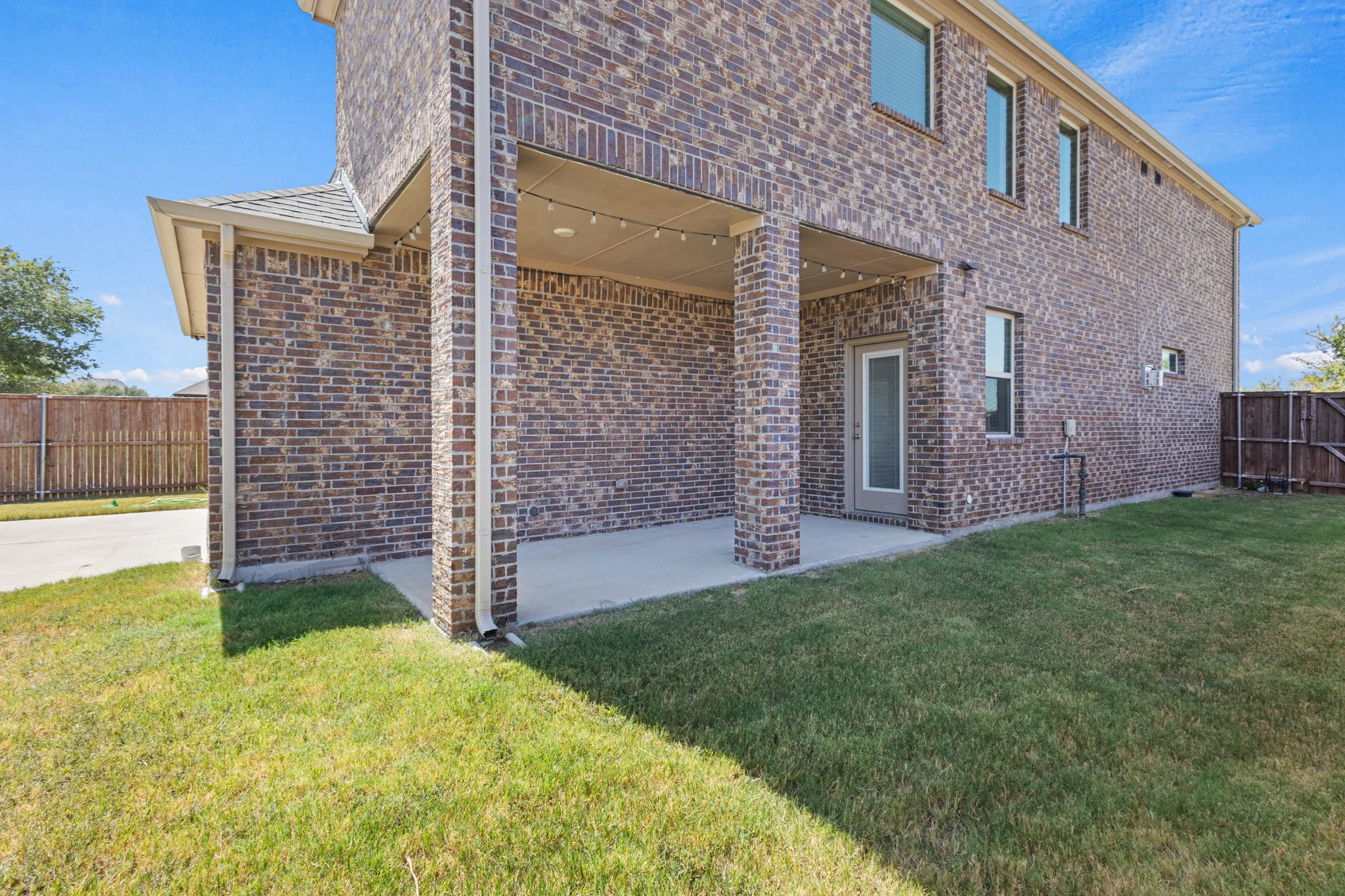 Brick exterior with a covered patio, concrete slab, and a grass lawn