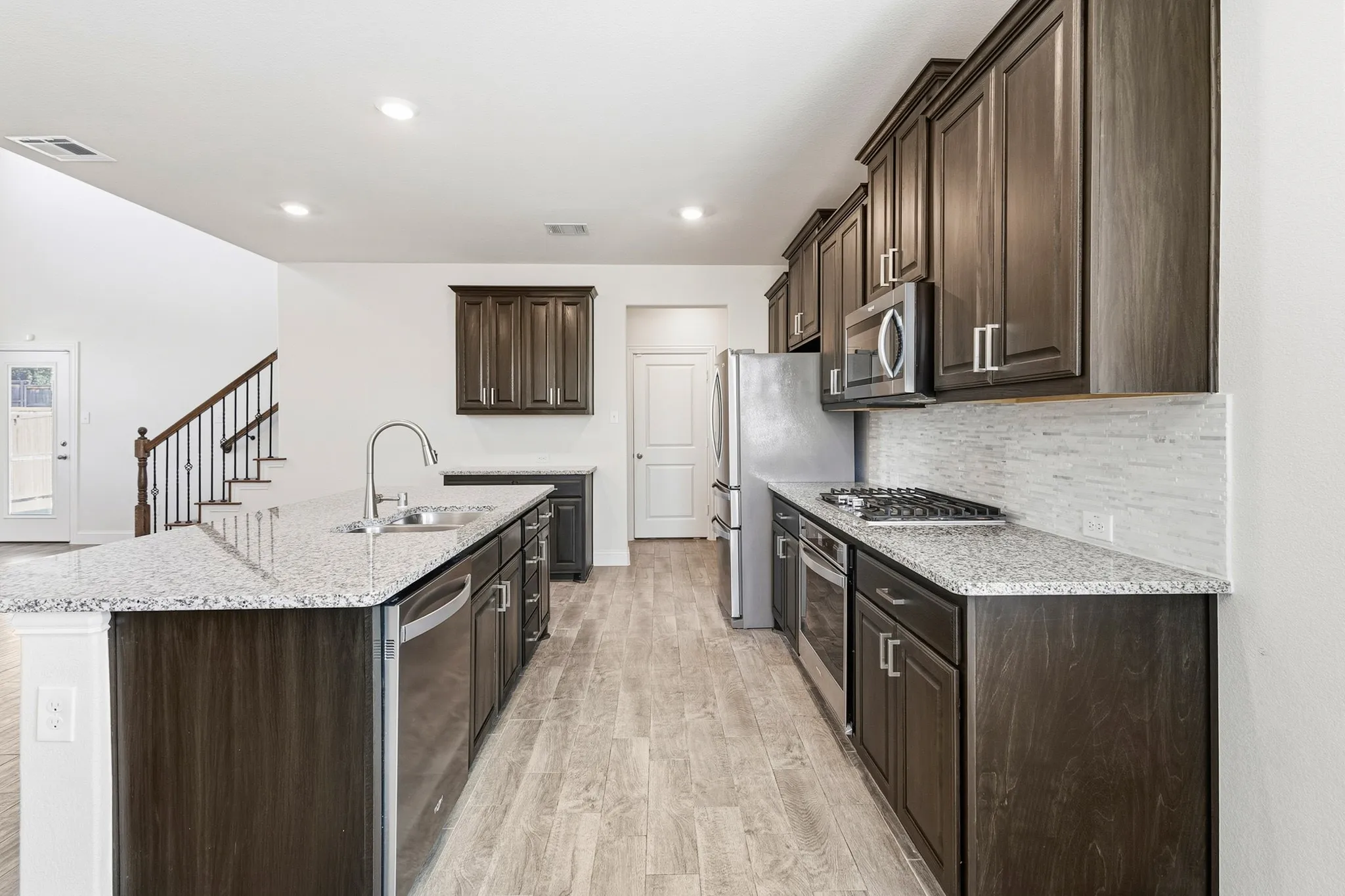 Kitchen featuring wood-finish cabinetry, stainless steel appliances, speckled countertops, and a tile backsplash