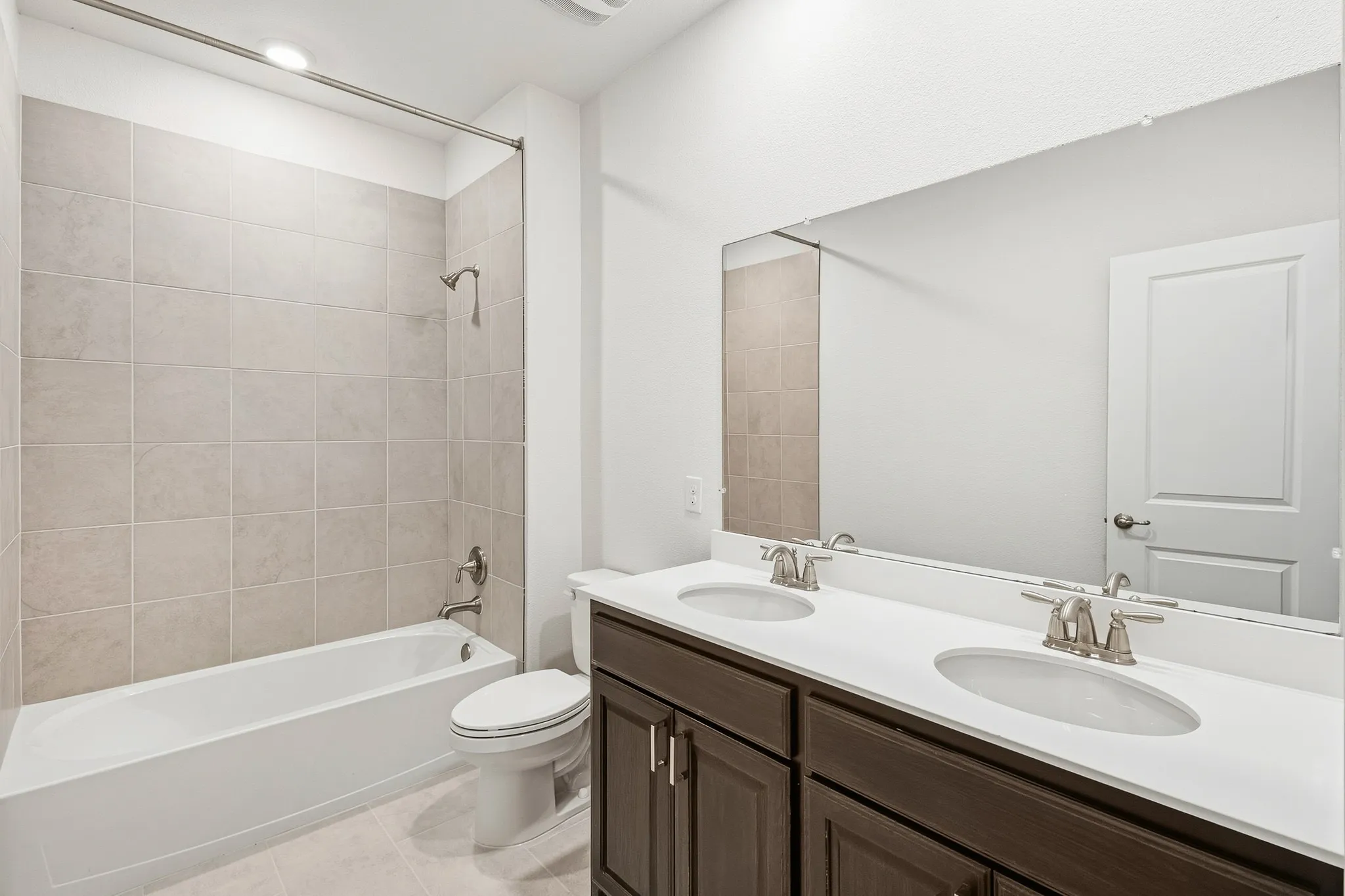 Bathroom featuring a dual-sink vanity with white countertop, dark wood-finish cabinetry, and a full-width mirror