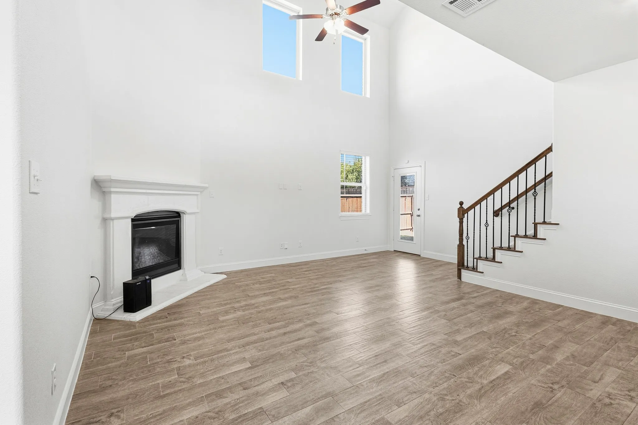 Vaulted ceilings, wood-finish flooring, corner fireplace with a white mantel, open-tread staircase with metal balusters, and a ceiling fan with light fixture