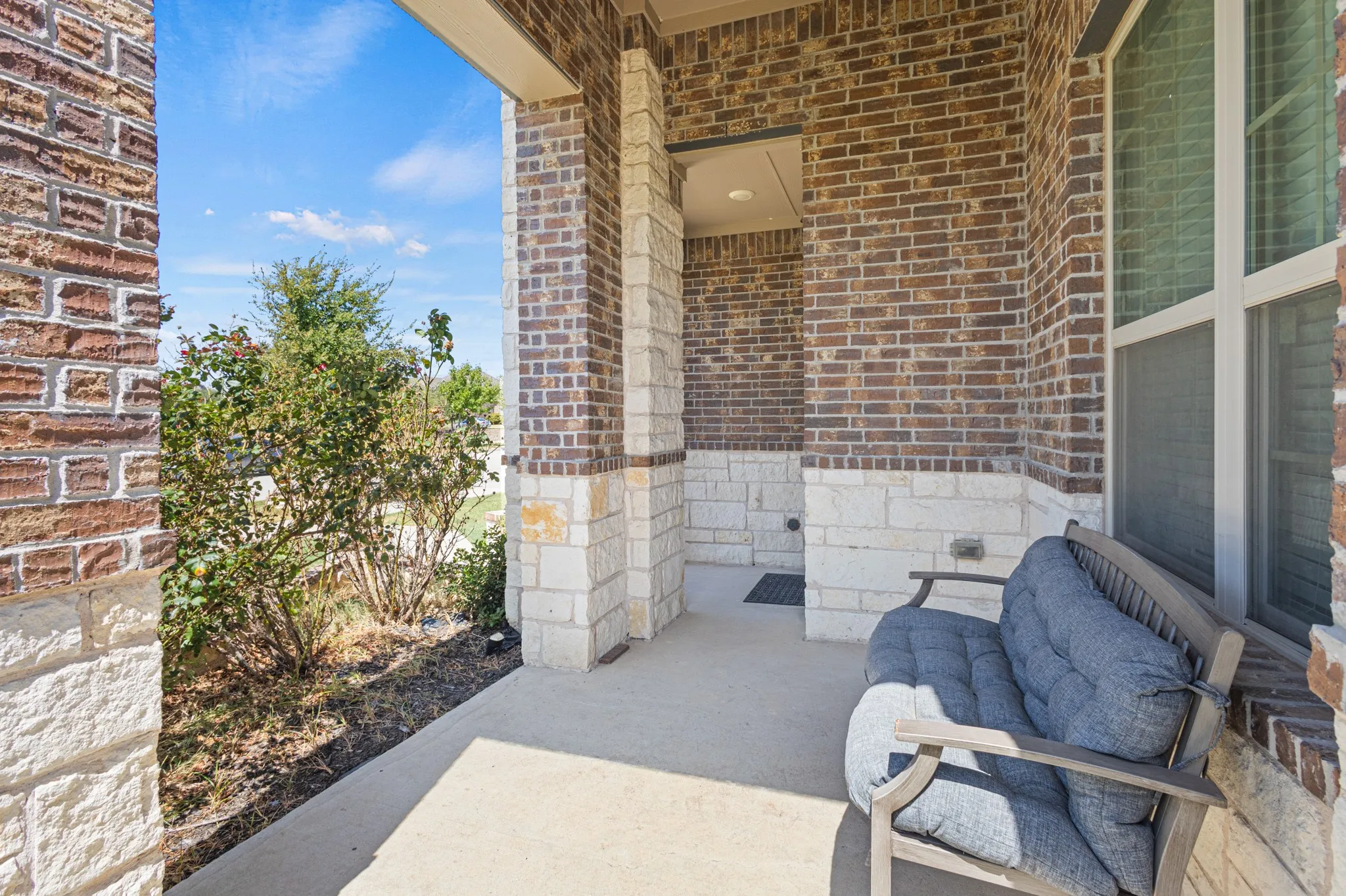 Covered porch with concrete flooring, brick and stone veneer walls, and a recessed entryway