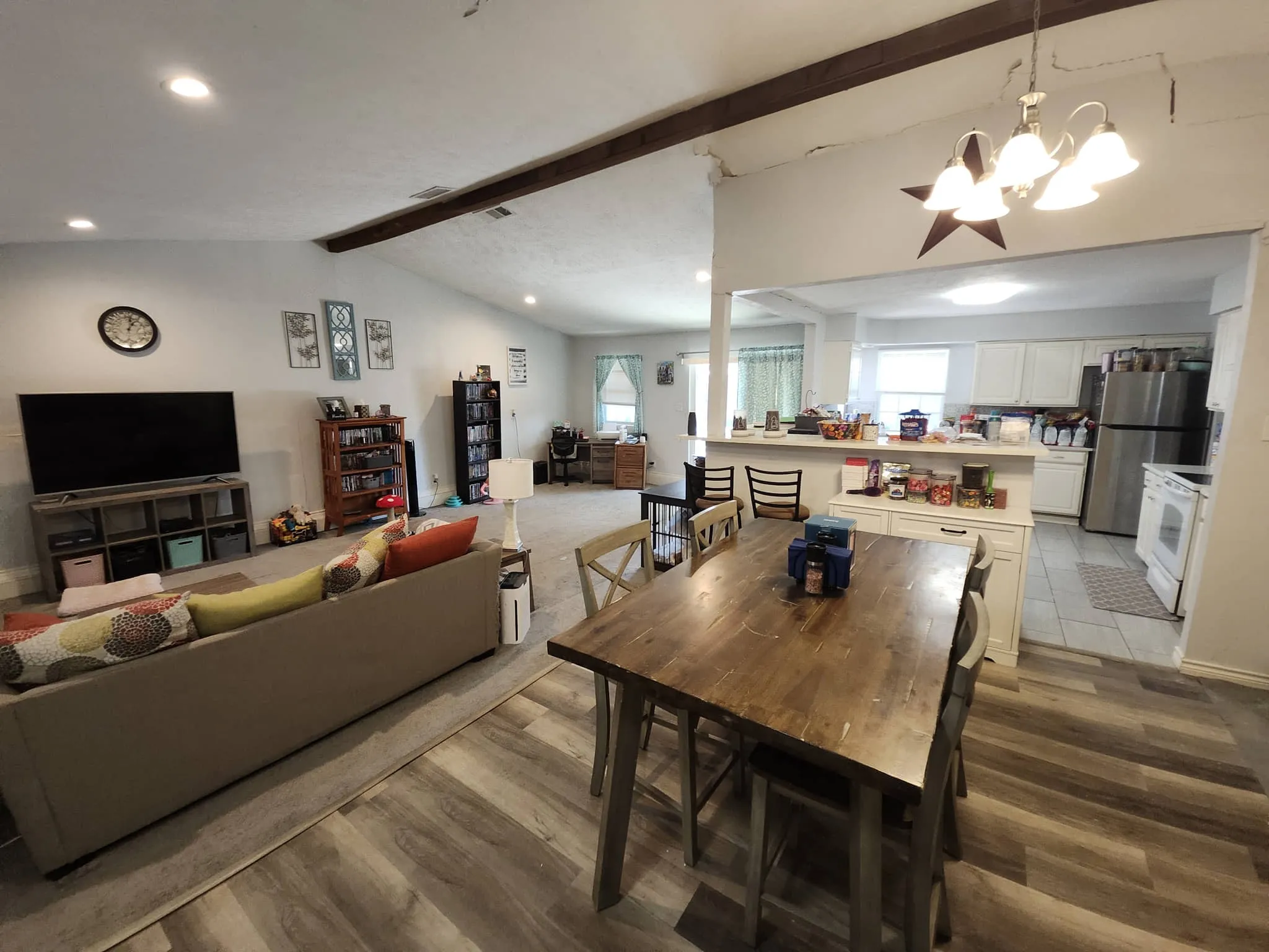 Vaulted ceilings with exposed wood beams, wood-finish flooring, recessed lighting, and a kitchen featuring white cabinetry and stainless steel appliances
