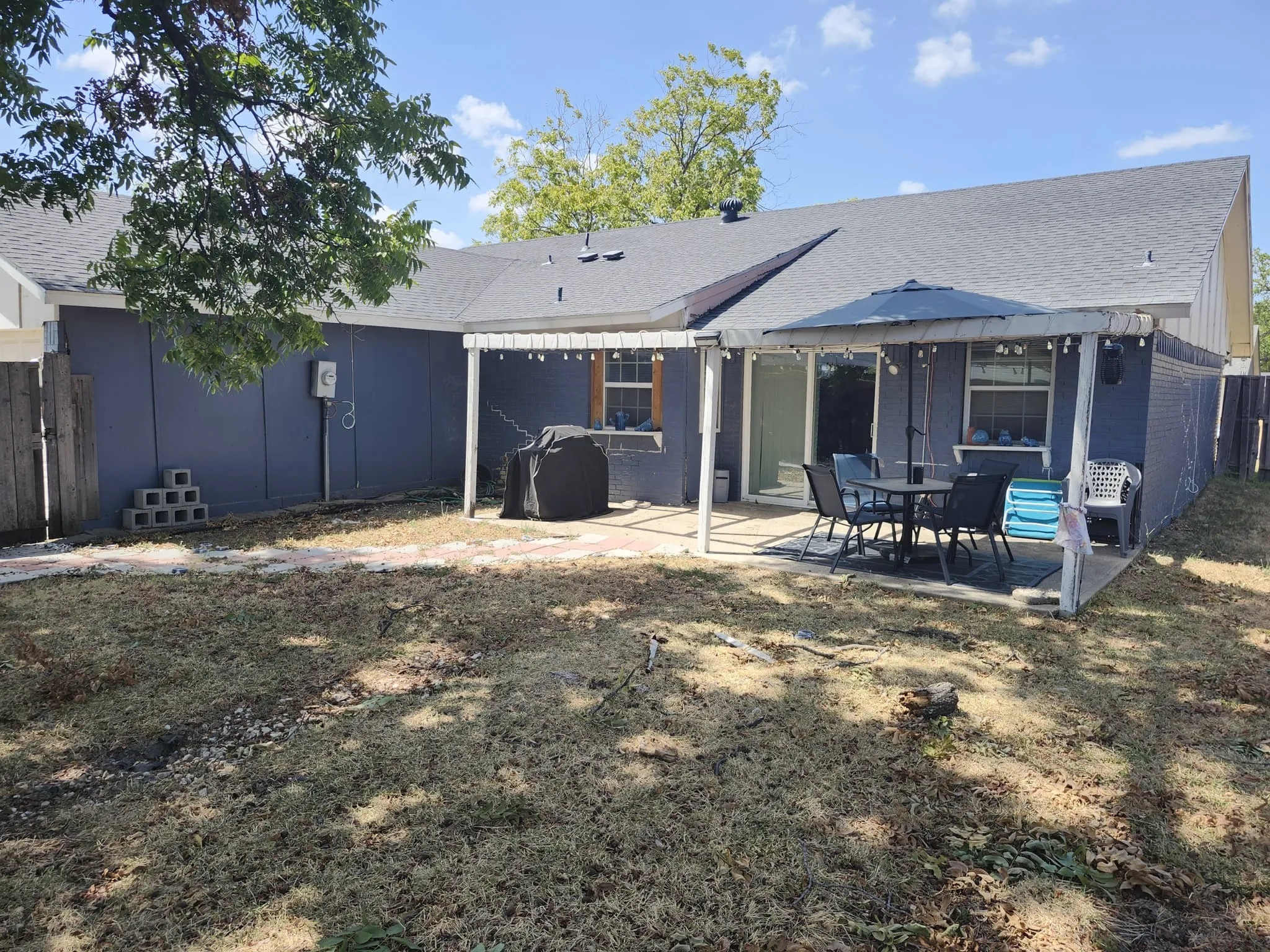 Expansive backyard featuring a covered patio, concrete slab, sliding glass door, and a privacy fence