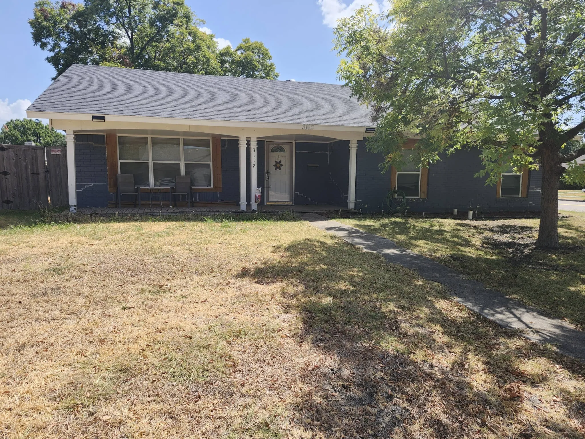 Front exterior featuring a covered porch with white columns, dark-painted siding, and a partial privacy fence