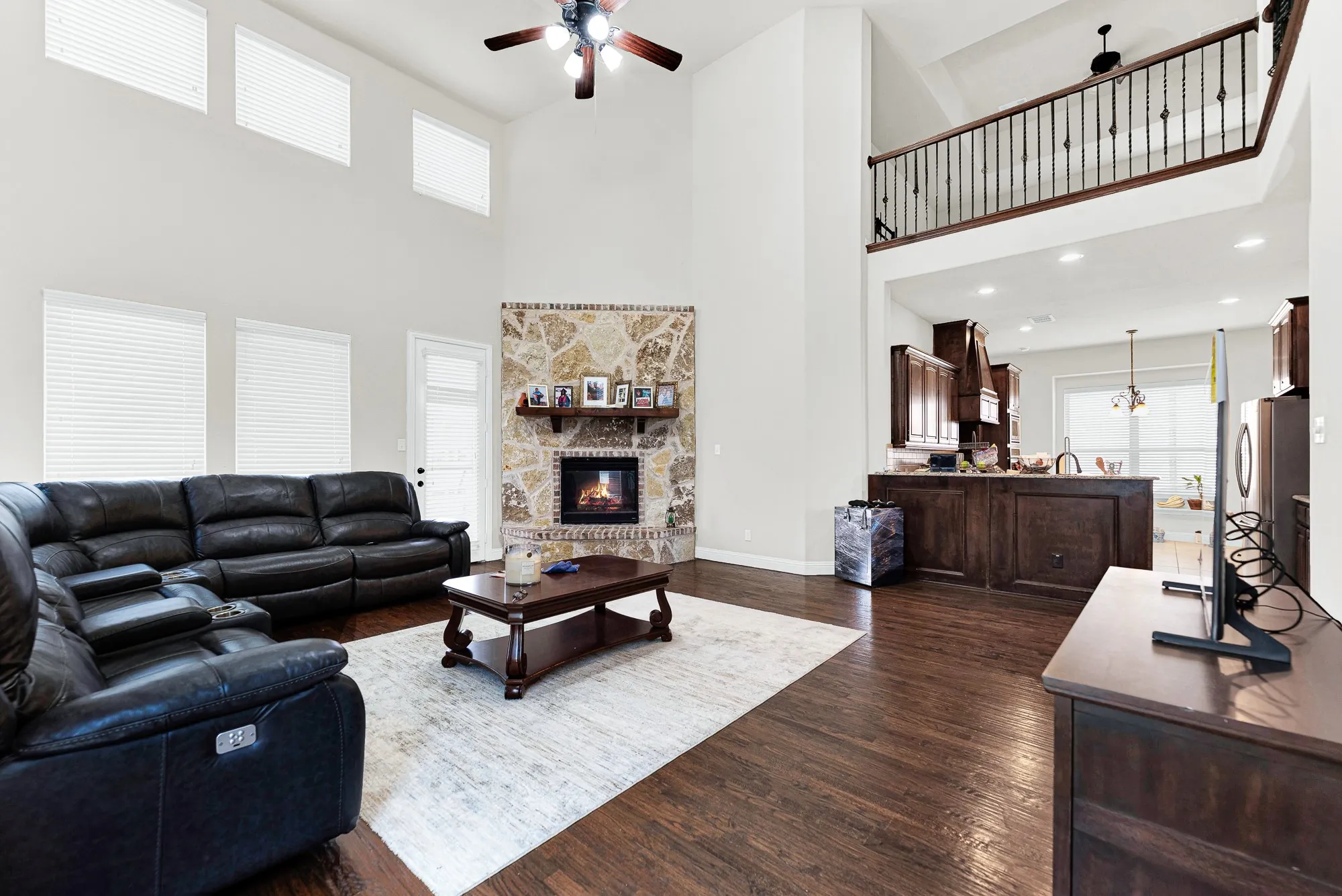 An upper-level wrought-iron overlook frames the room, connecting the open living area seamlessly to the kitchen space below. It is the perfect setup for throwing open the doors and hosting easy weekend get-togethers with friends