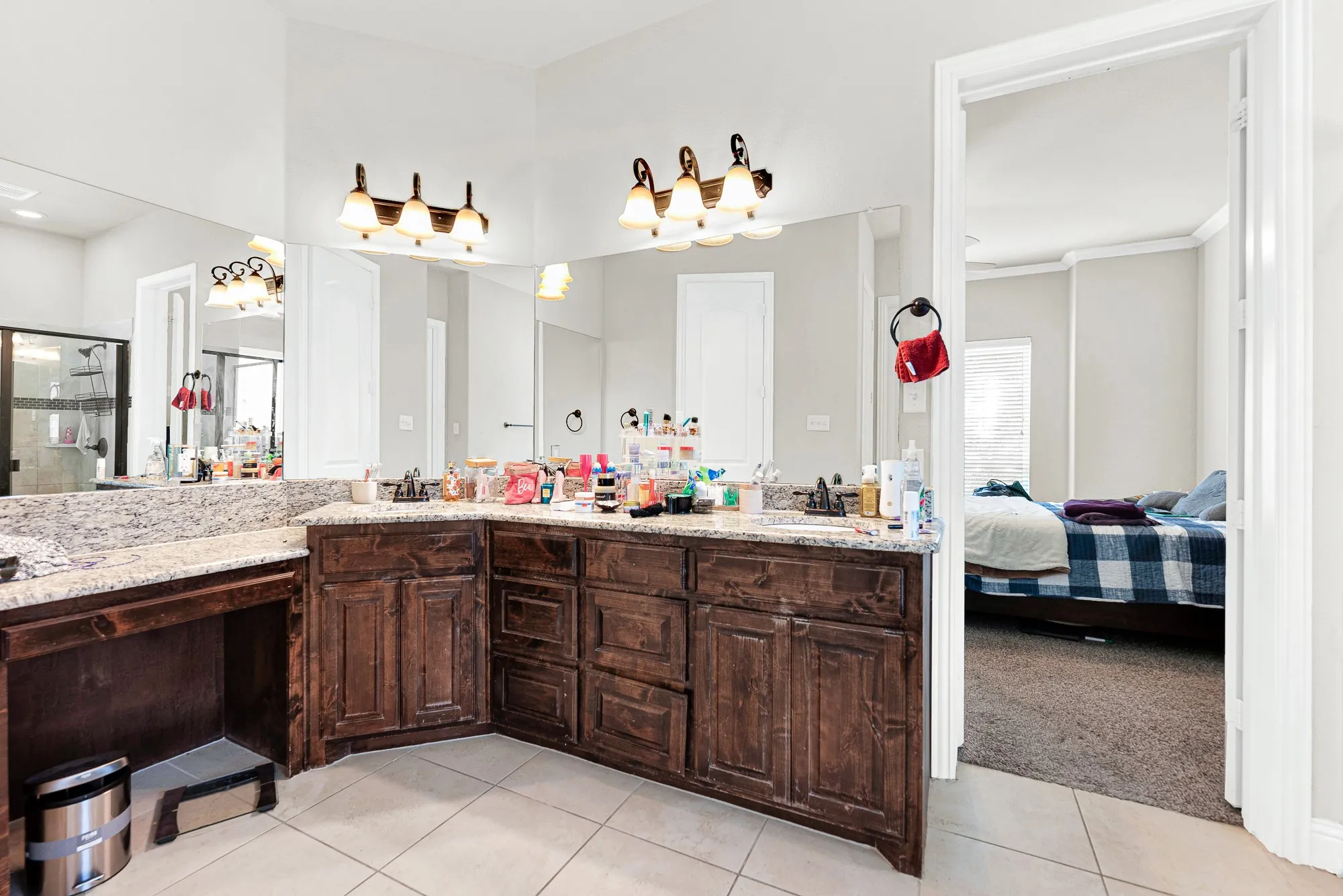 An expansive L-shaped vanity setup topped with granite offers dual sinks and an integrated vanity seating area under bright, warm lighting. You will love having your own space to comfortably prep and unwind during busy morning routines.