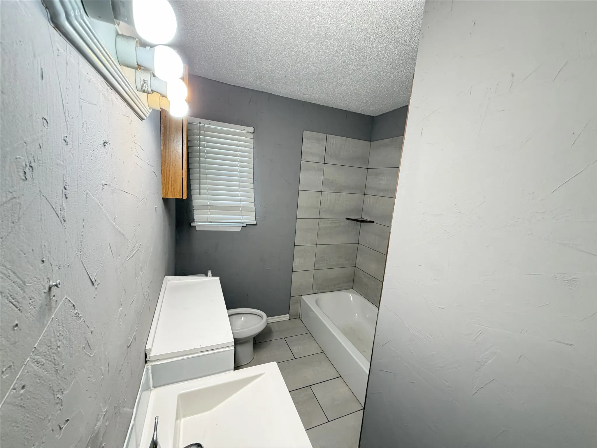 Built-in vanity with integrated sink, adjacent toilet, bath/shower combination with tiled surround, and wood-finish wall cabinet