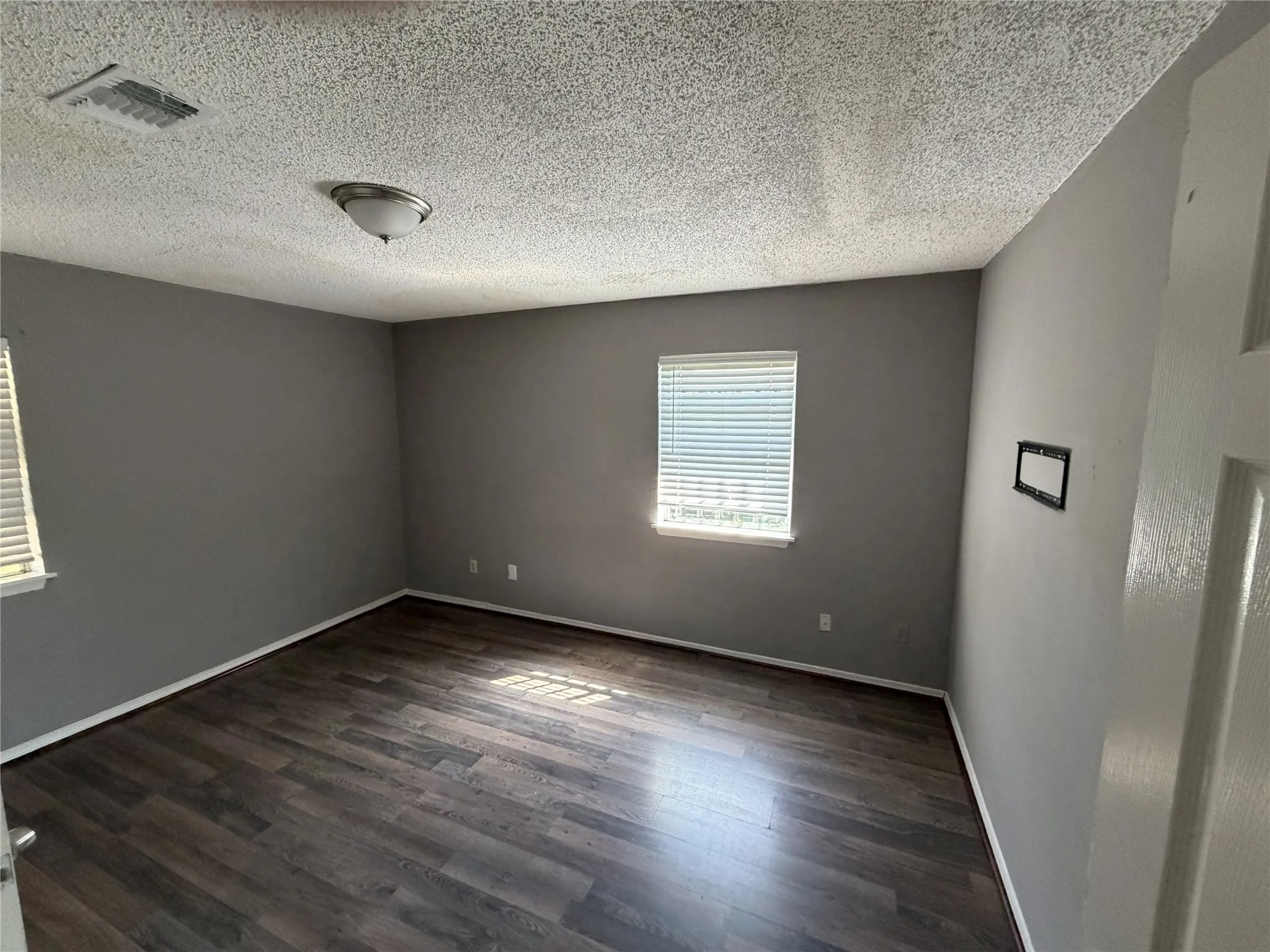 Dark wood-finish flooring, neutral gray wall paint, and windows with horizontal blinds