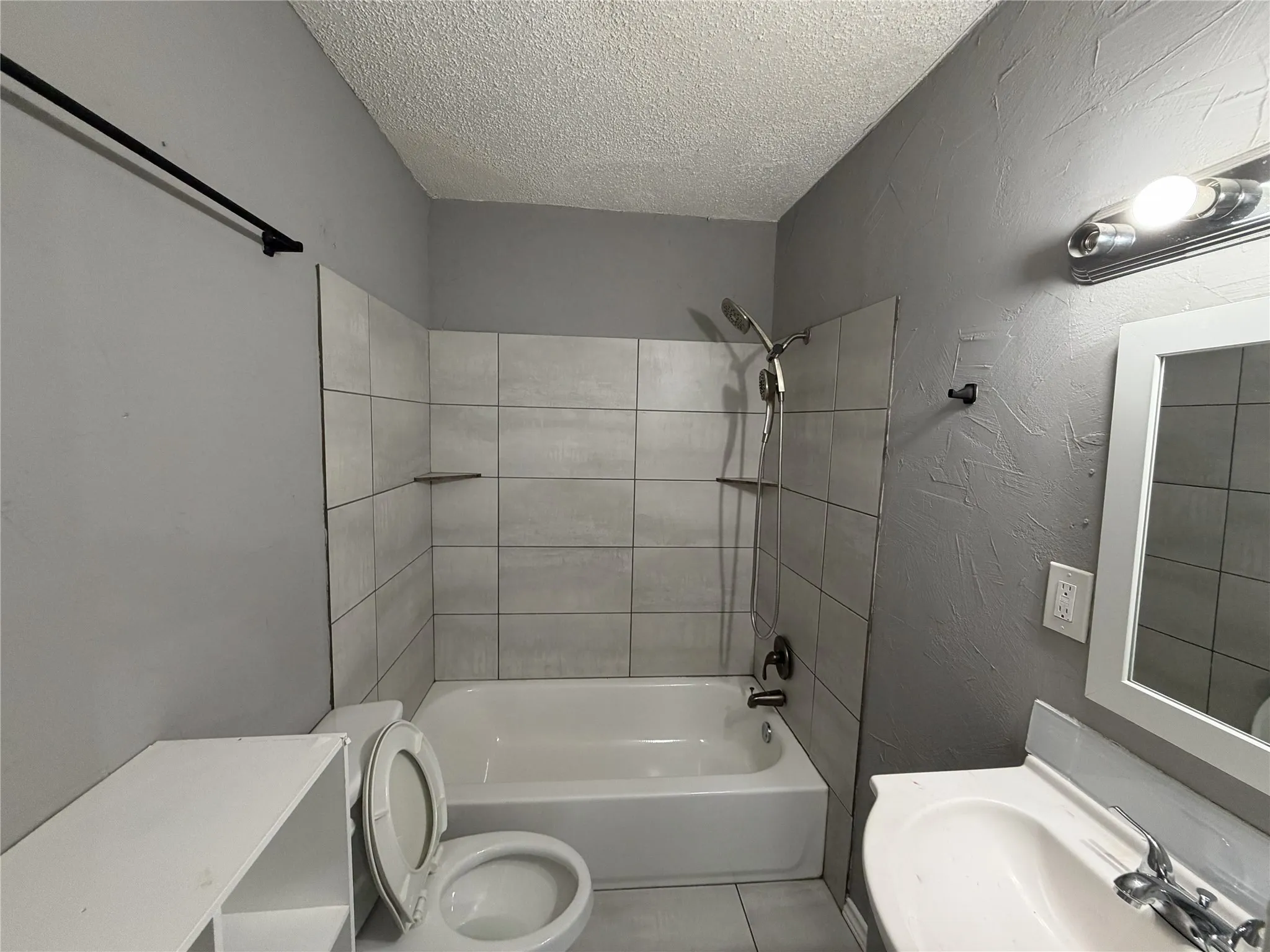 White bathtub with tiled shower surround, wall-mounted showerhead, and built-in shelving