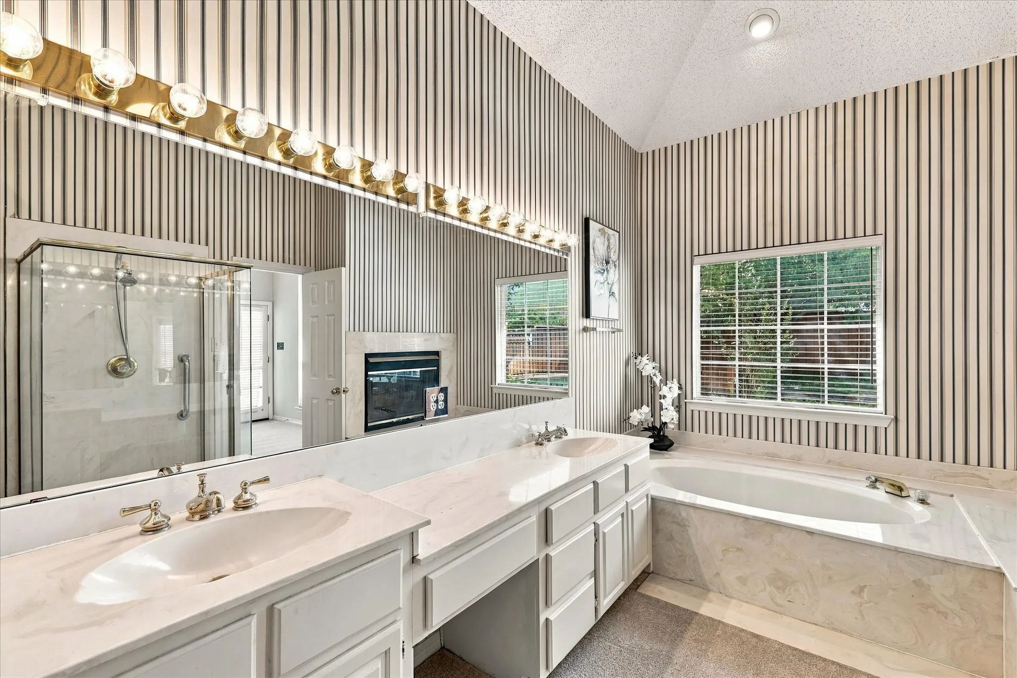 Dual vanity with undermount sinks, built-in soaking tub, glass-enclosed shower, built-in fireplace, and vaulted ceiling