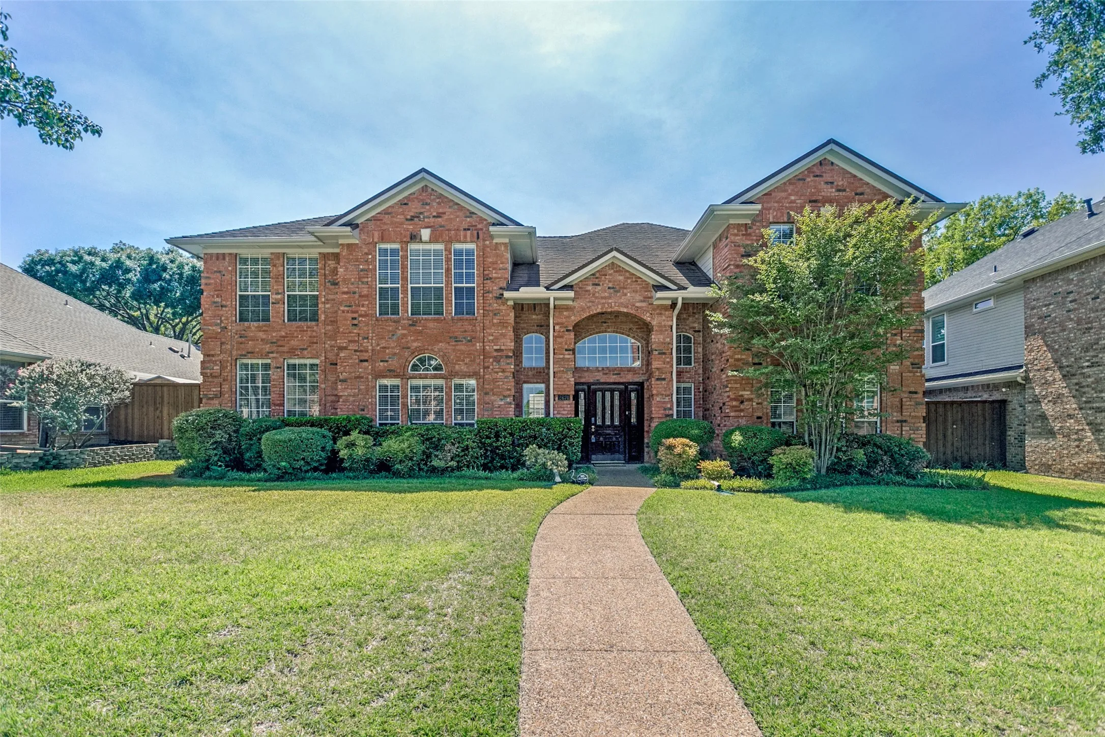 Brick facade with a gabled roofline, arched entry window, decorative front door, and a paved walkway