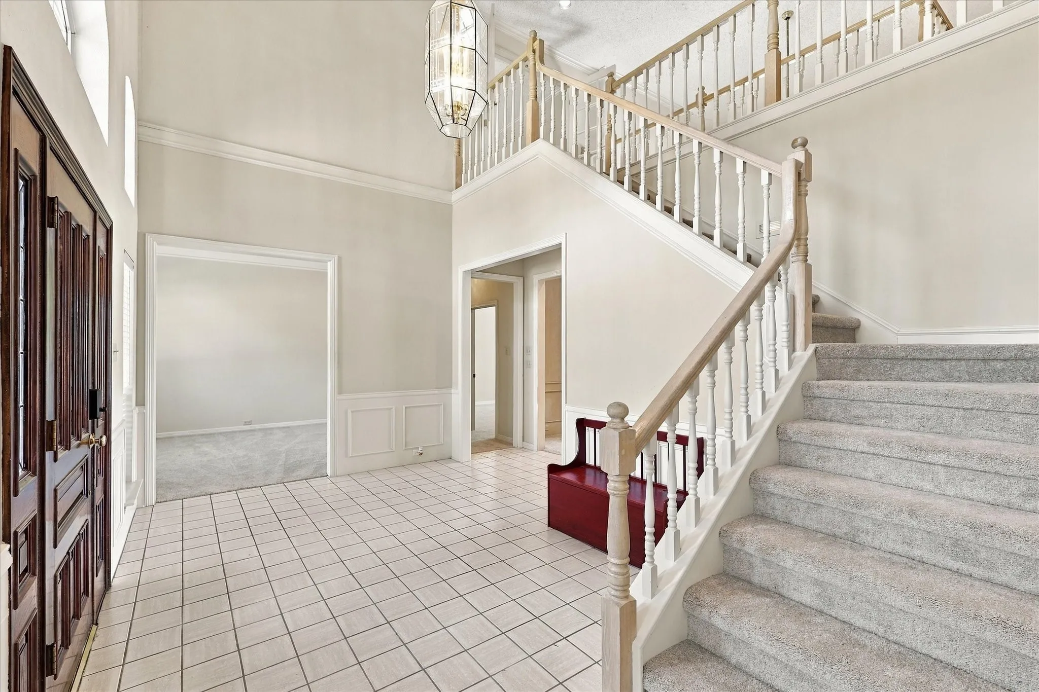 Two-story foyer featuring tile flooring, a dark wood-finish entry door, a grand staircase with carpeted treads and wood handrails, wainscoting, and a multi-tiered chandelier