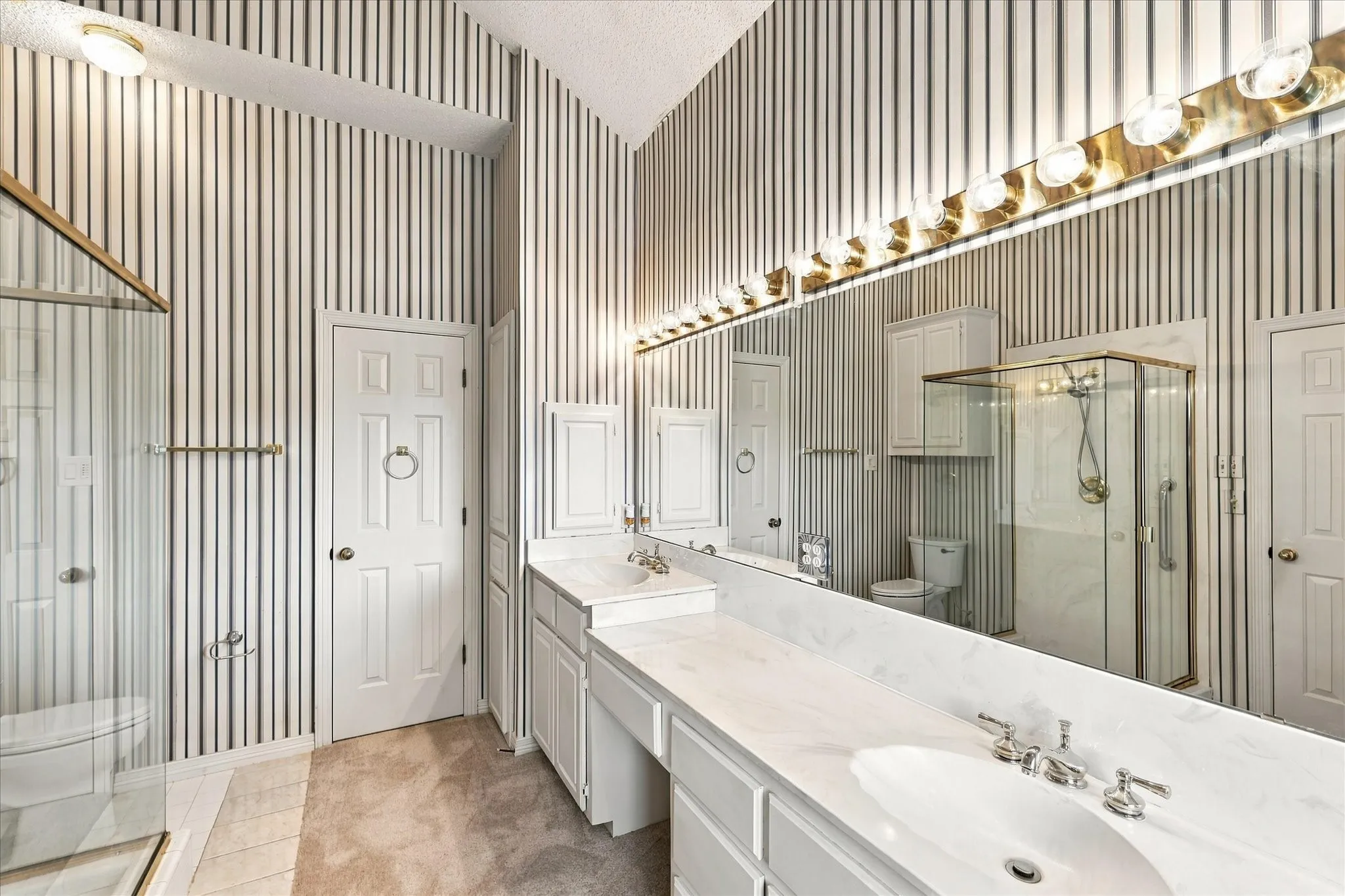 Dual vanity with undermount sinks, glass-enclosed shower, built-in cabinetry, and wall-mounted lighting