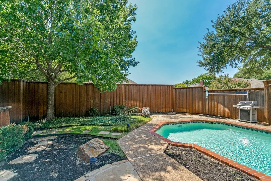 Outdoor swimming pool with brick coping, surrounding concrete patio, and a wood privacy fence