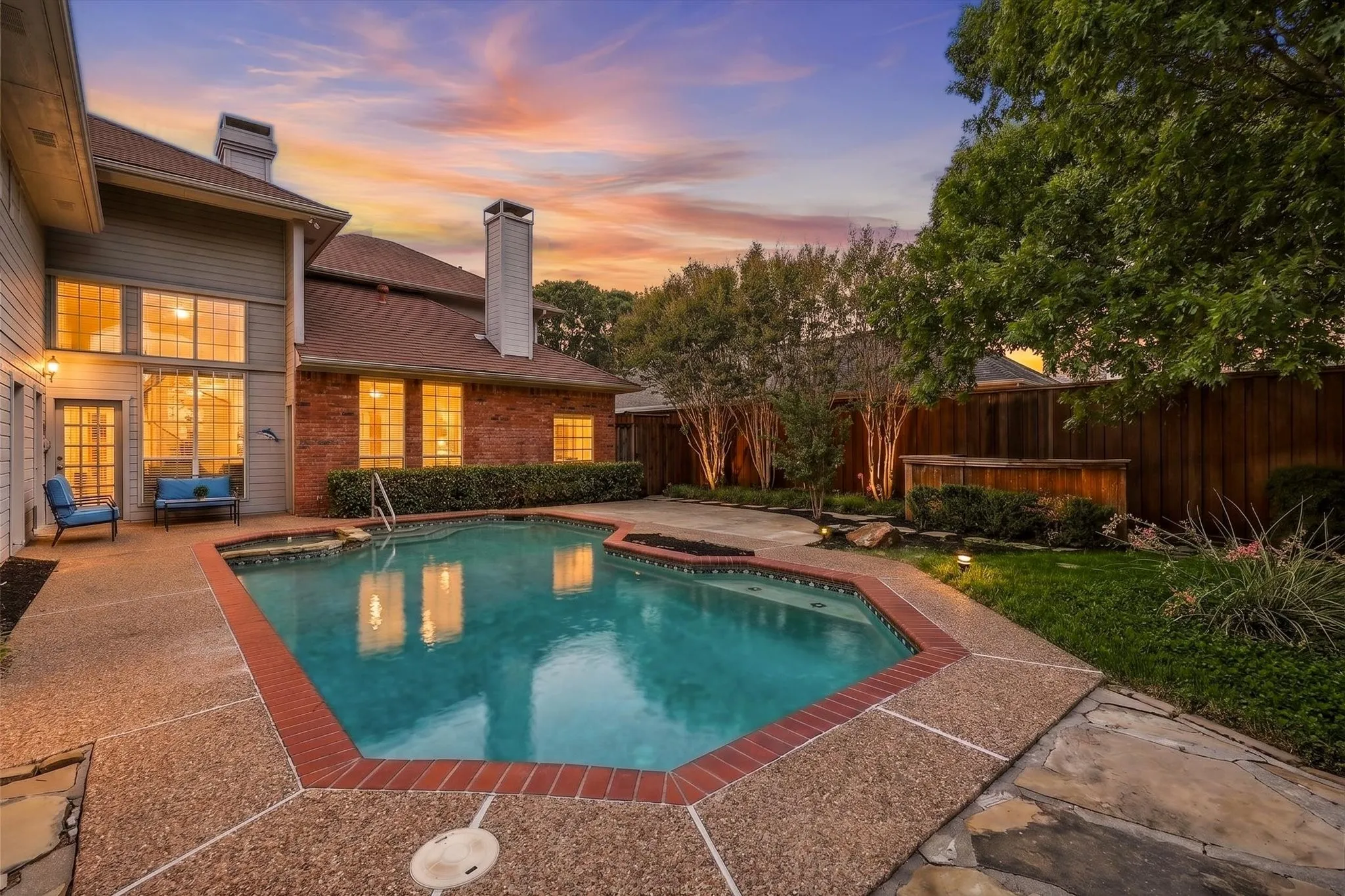 In-ground swimming pool with integrated spa, bordered by a textured concrete patio and red brick coping