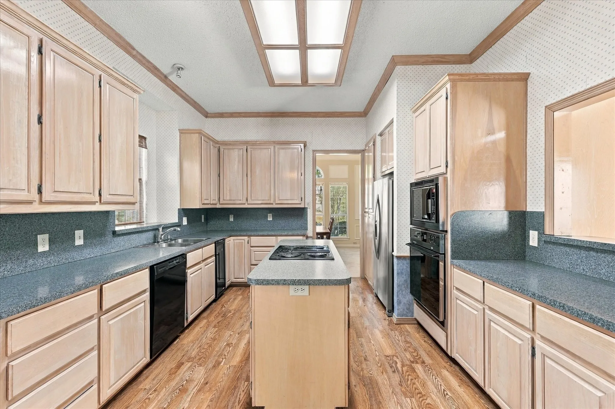 Kitchen featuring extensive light wood cabinetry, stone-finish countertops, wood-finish flooring, and a central island with cooktop