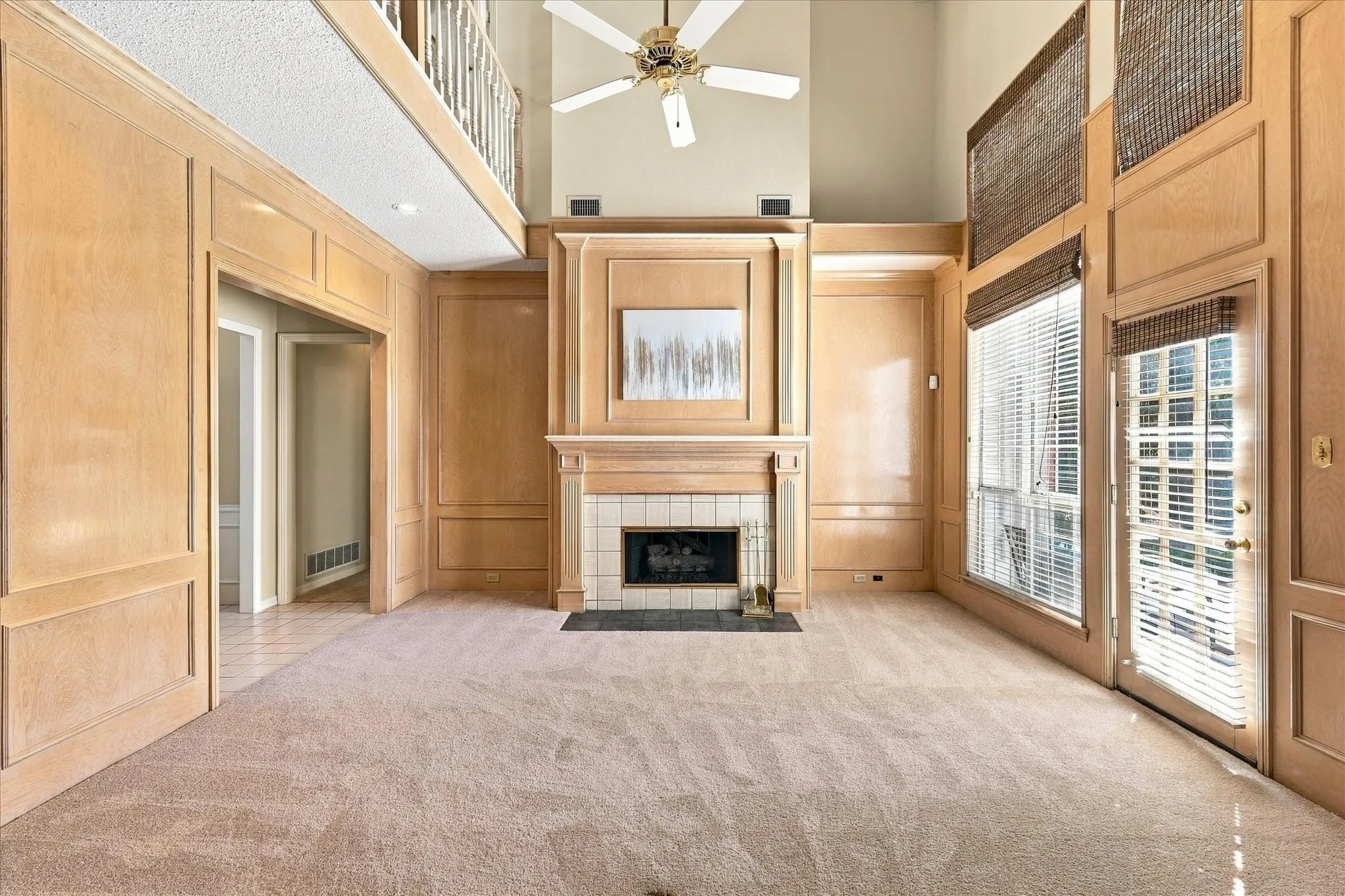 Vaulted ceiling with ceiling fan, fireplace with tile surround, wood paneling, and a balcony overlook