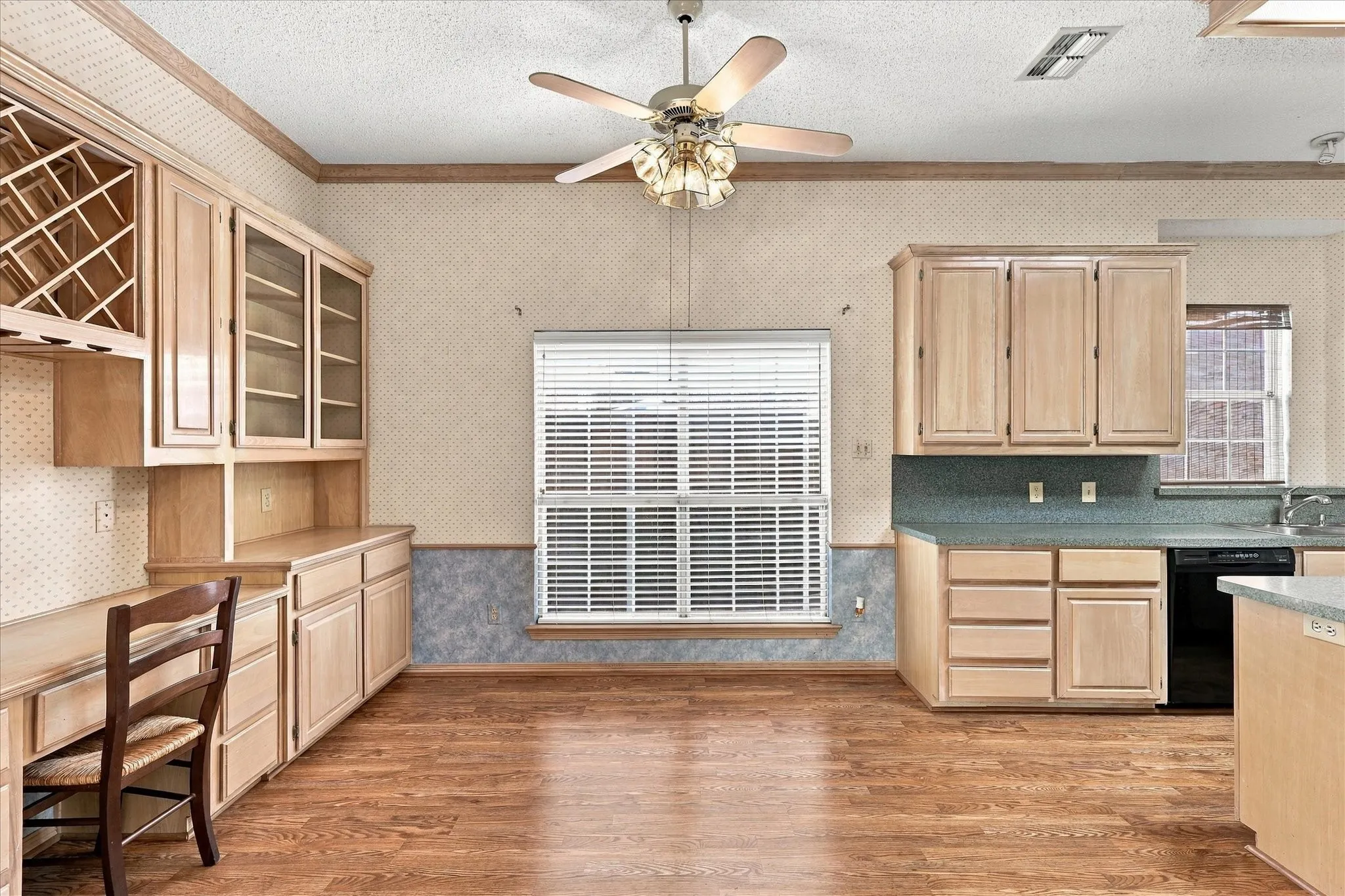 Wood-finish flooring, built-in cabinetry with glass-front uppers, integrated wine rack, ceiling fan, and window with blinds