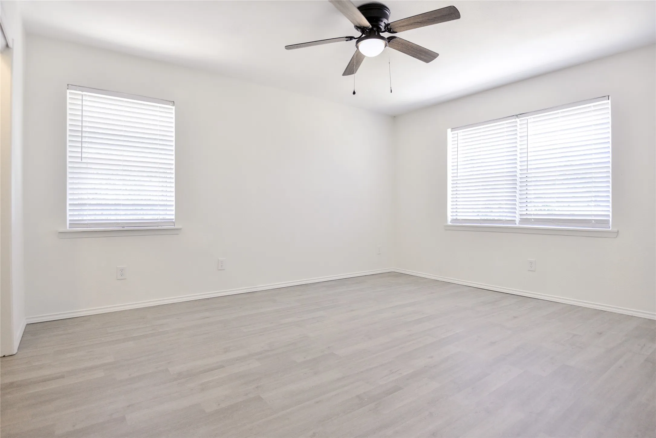 Spacious room featuring light wood-finish flooring, white walls, and a ceiling fan with integrated lighting