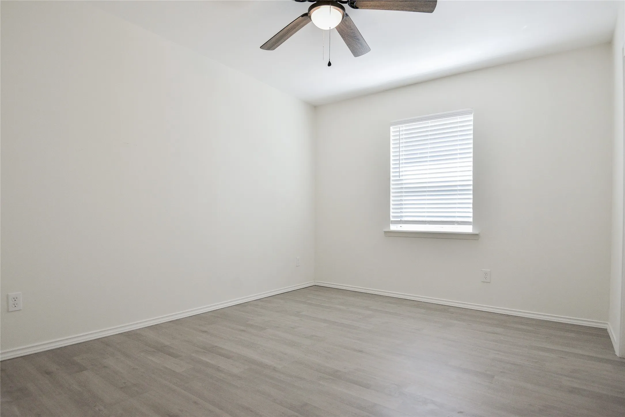 Wood-finish flooring, white walls, and a window with blinds