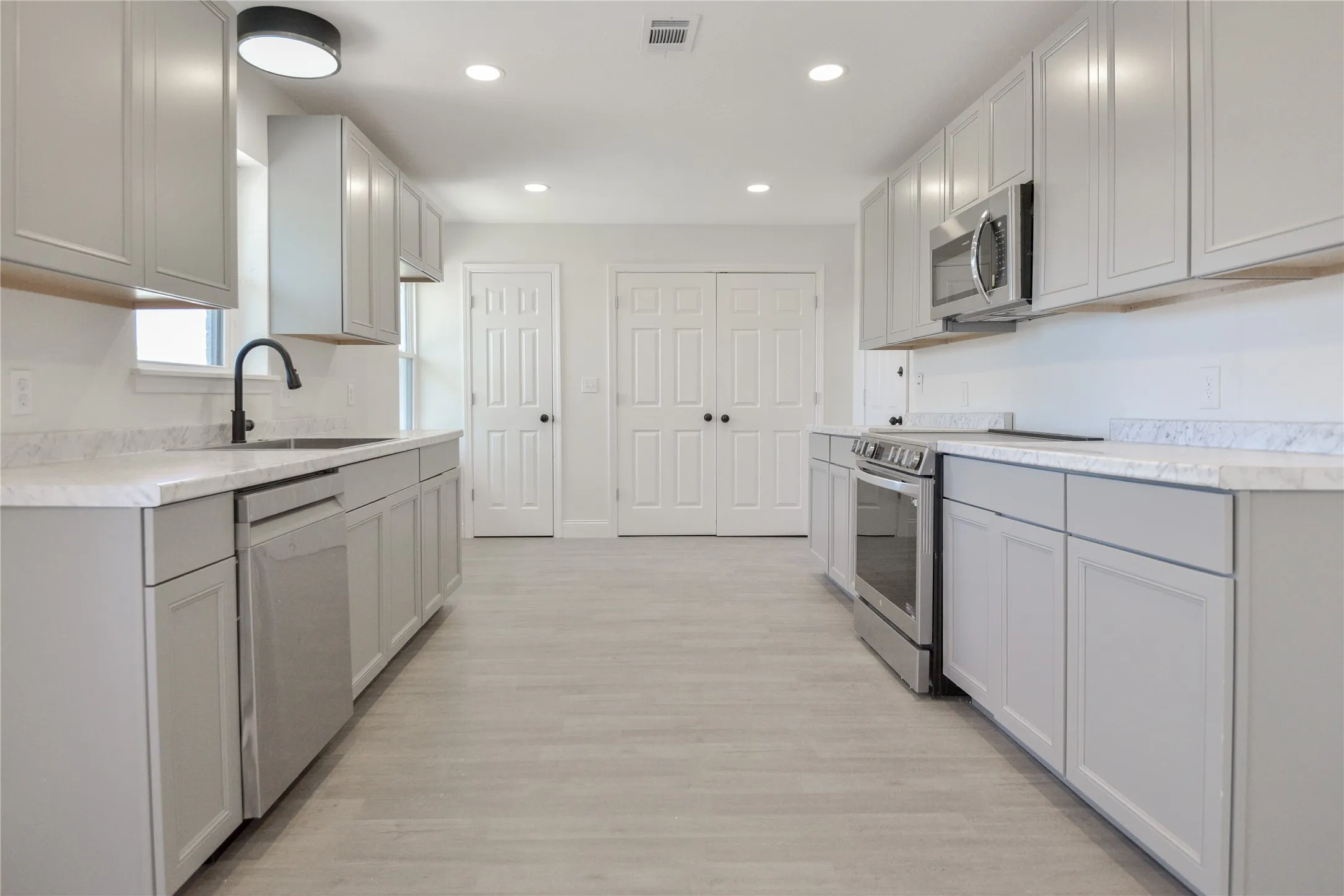 Kitchen featuring light gray cabinetry, stainless steel appliances, light-toned countertops, and wood-finish flooring