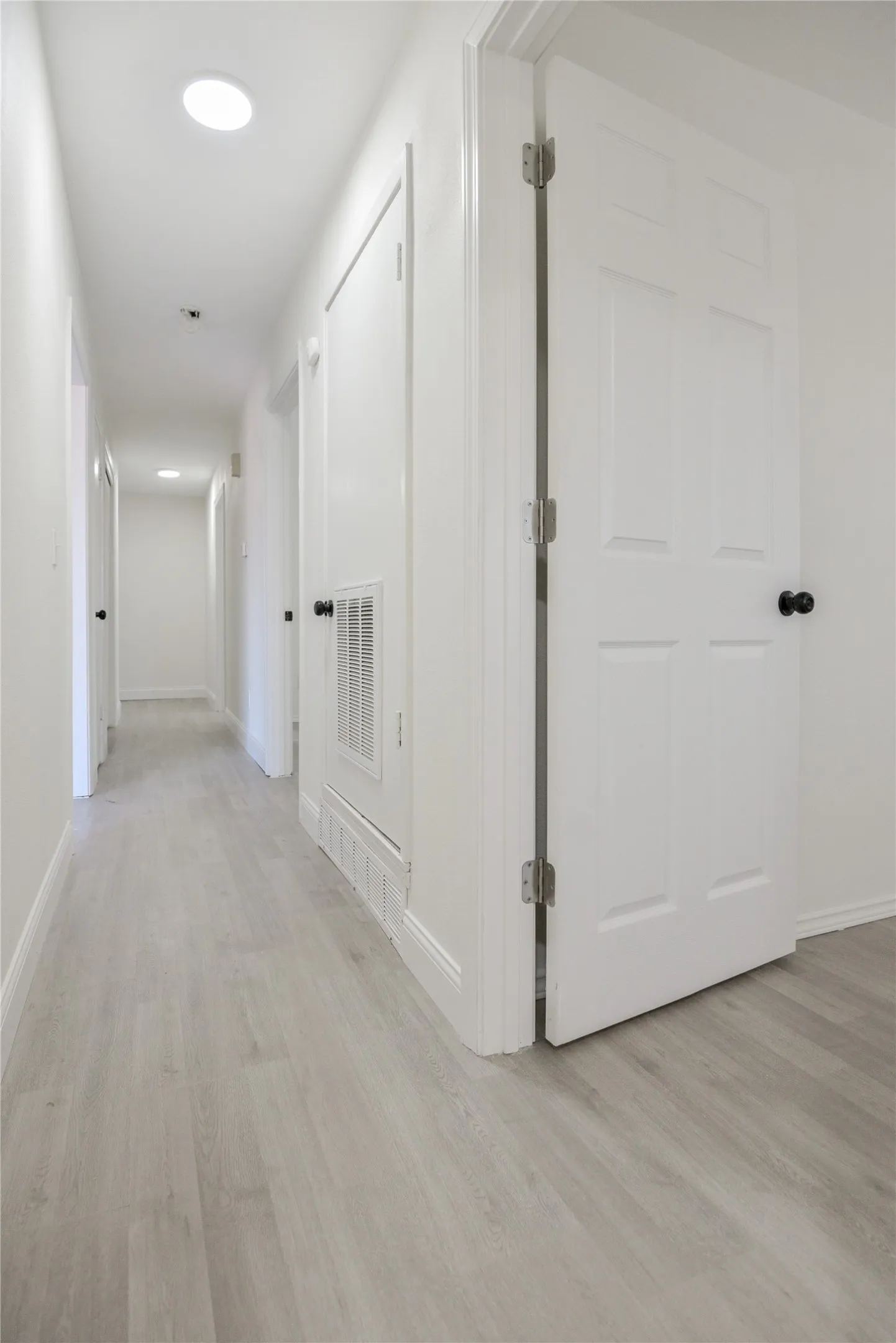 Hallway featuring recessed lighting, wood-finish flooring, white paneled doors, and contemporary black door hardware