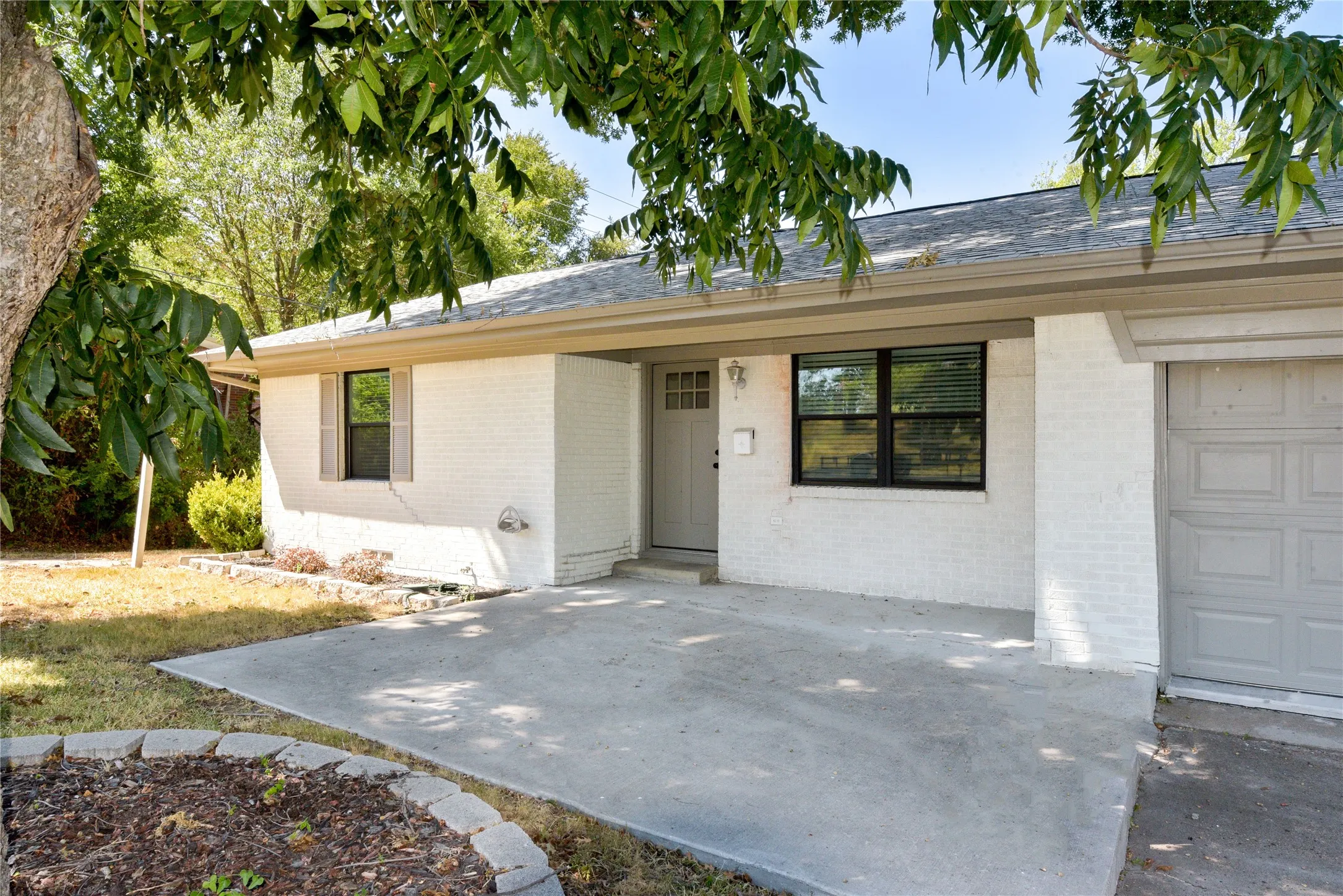 White brick exterior with a light-toned entry door, single-pane windows, and an attached garage