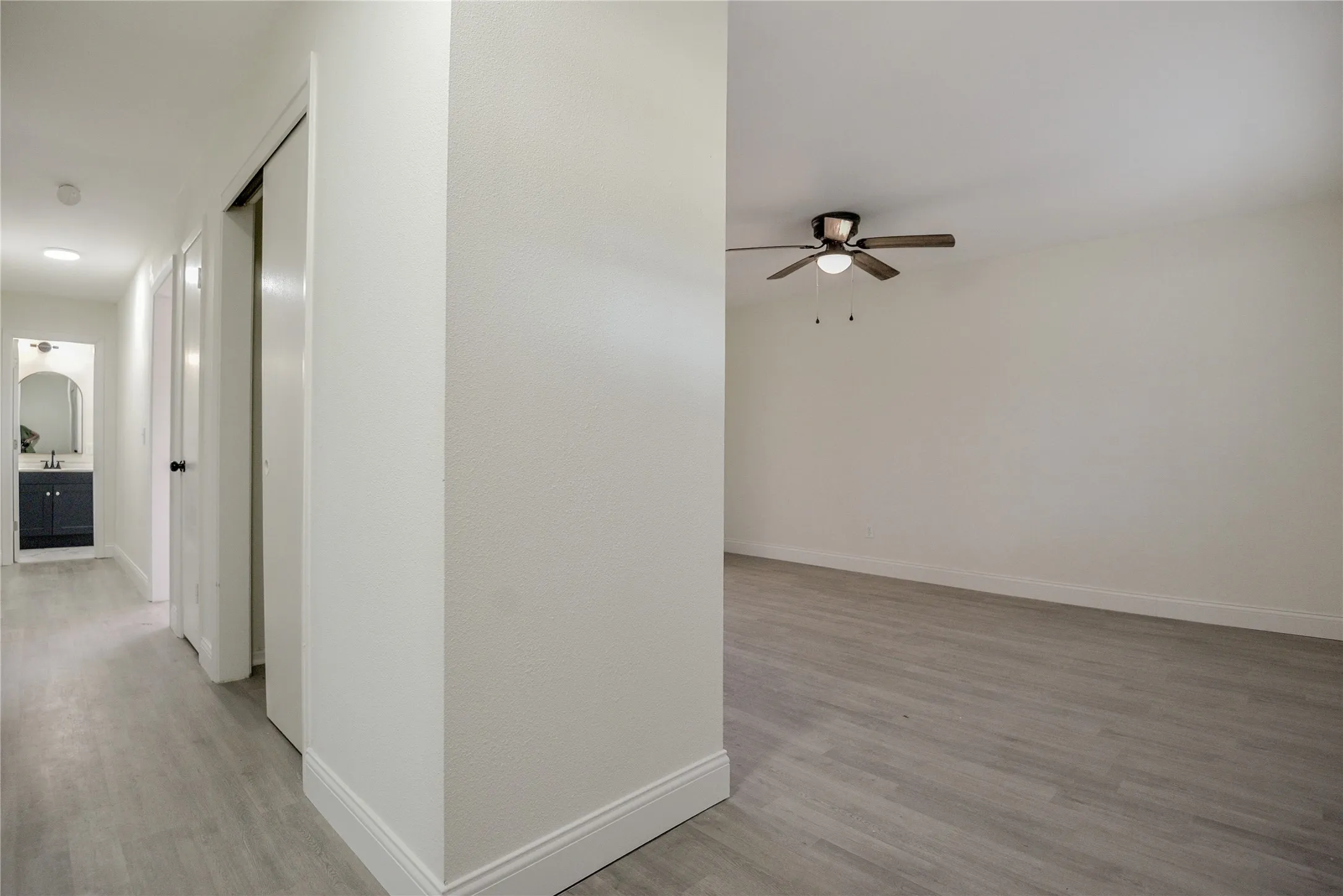 Wood-finish flooring throughout, ceiling fan with integrated lighting, and a hallway vanity with dark cabinetry