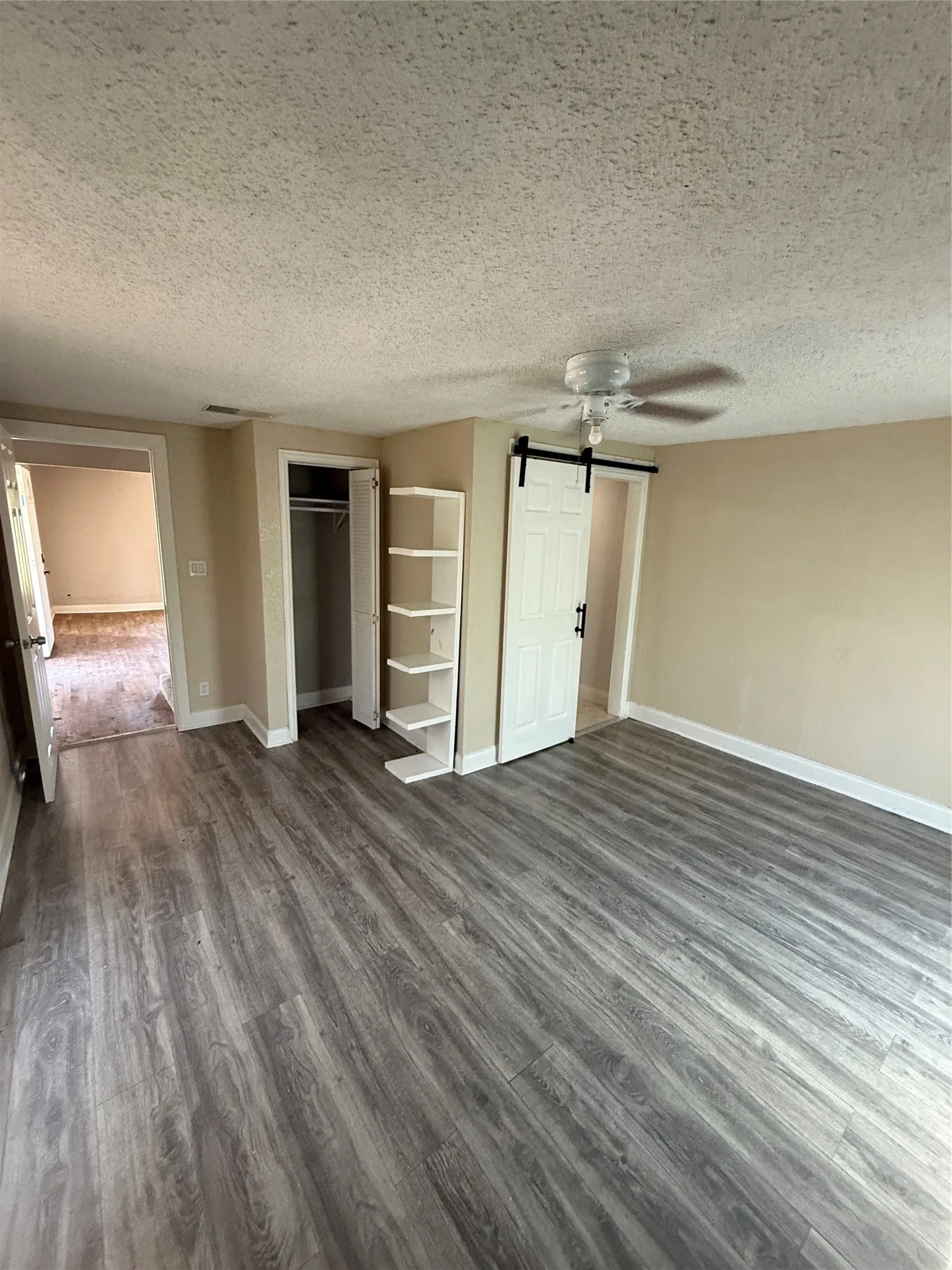 Wood-finish flooring, built-in shelving, ceiling fan, and barn door