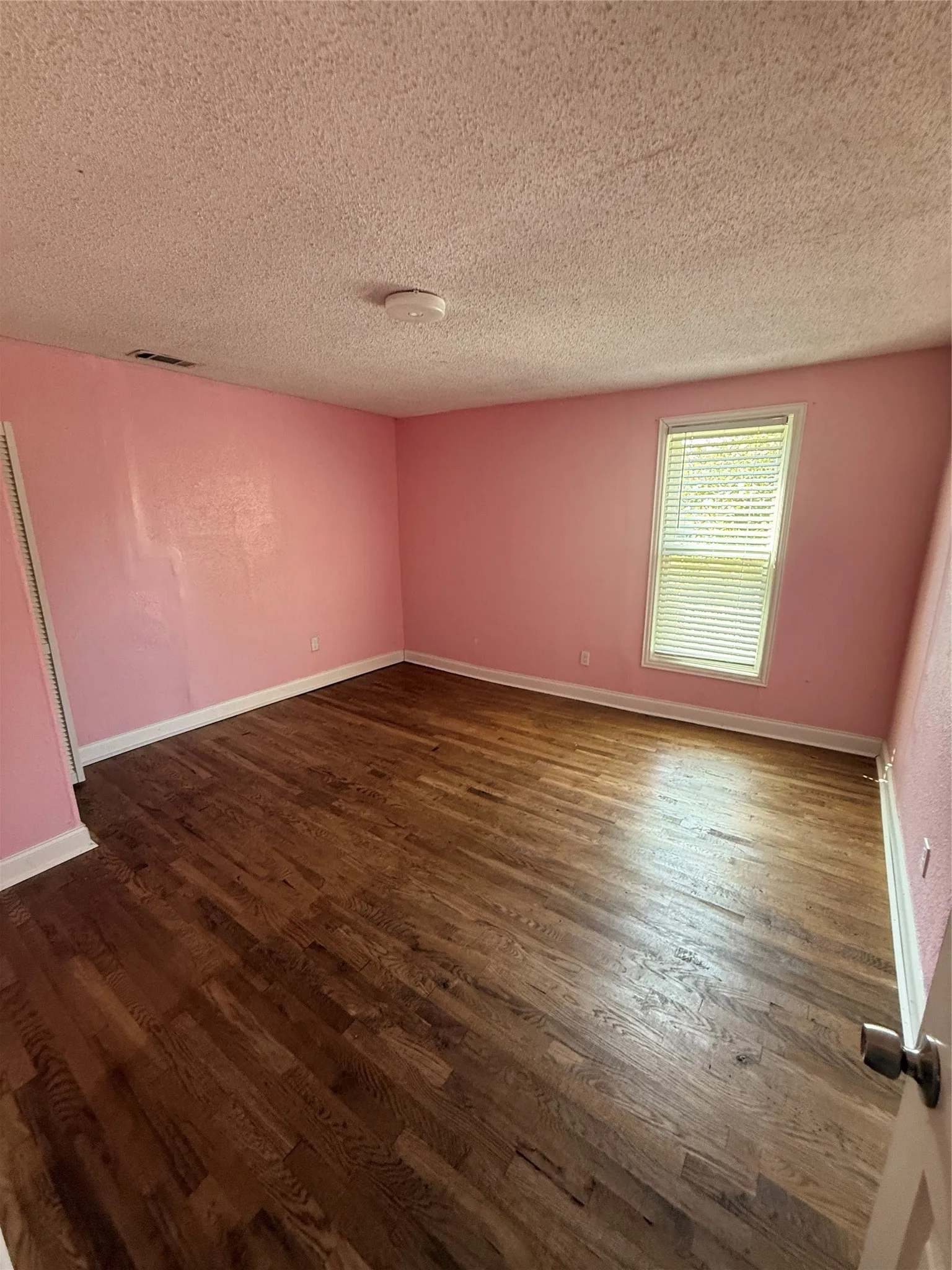 Hardwood-style flooring with white trim and a single window with blinds