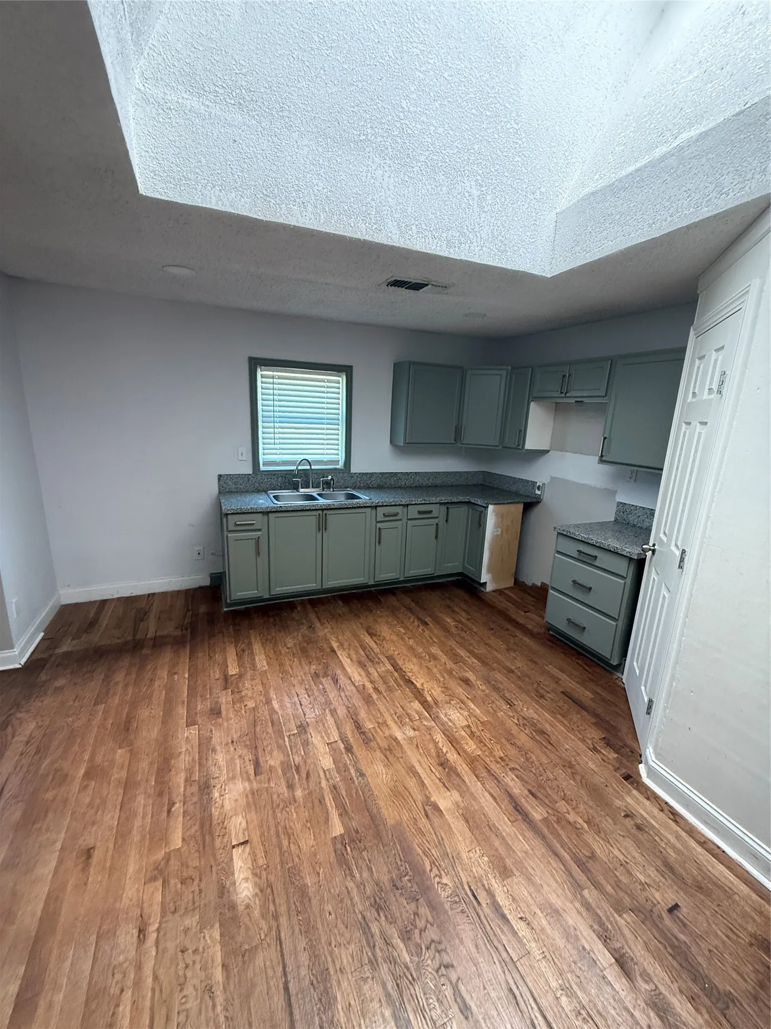 Kitchen featuring wood-finish flooring, sage-colored cabinetry, granite-look countertops, and a stainless steel double basin sink