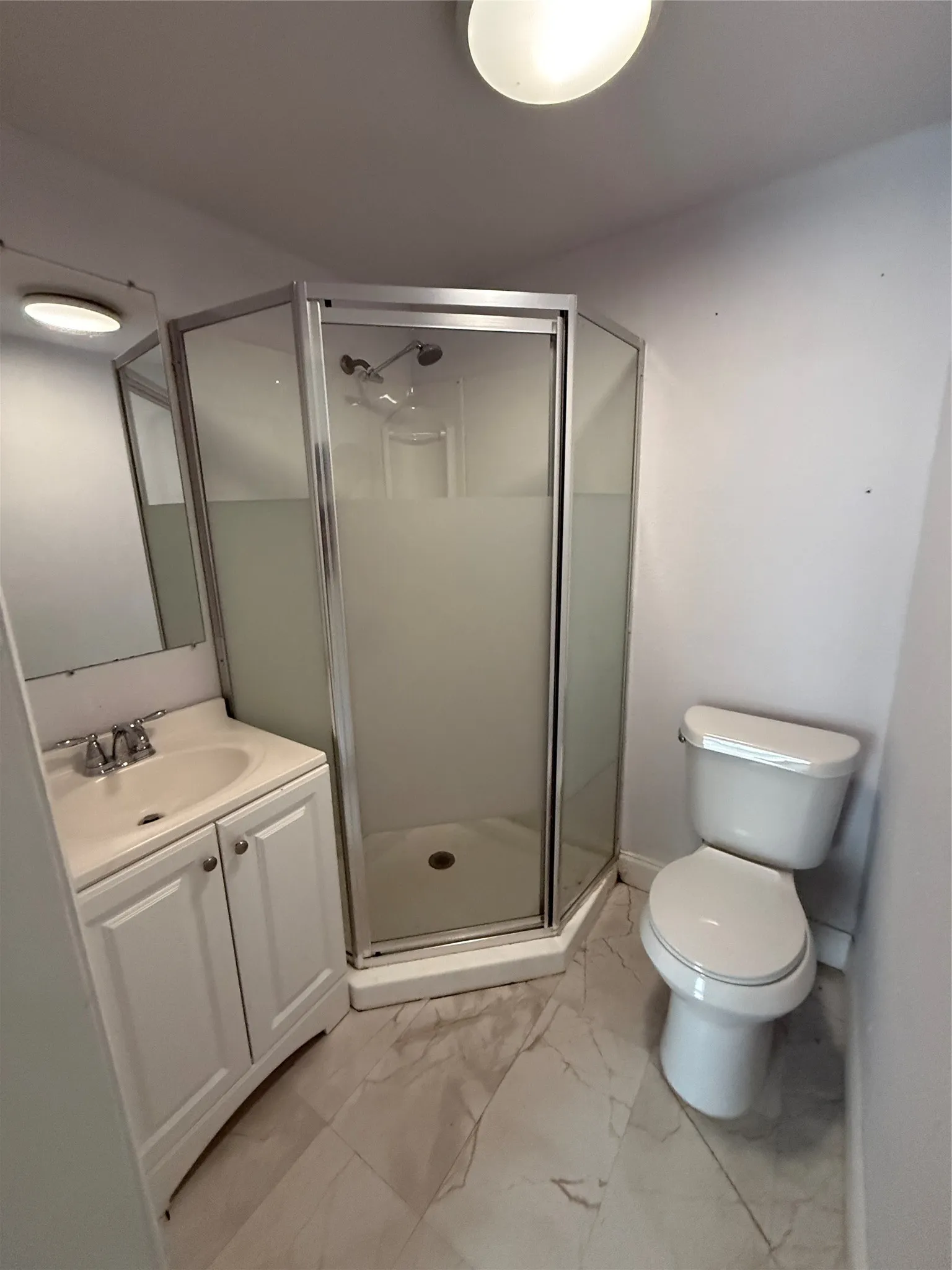 Vanity with an integrated sink, corner shower enclosure with frosted glass, and a toilet